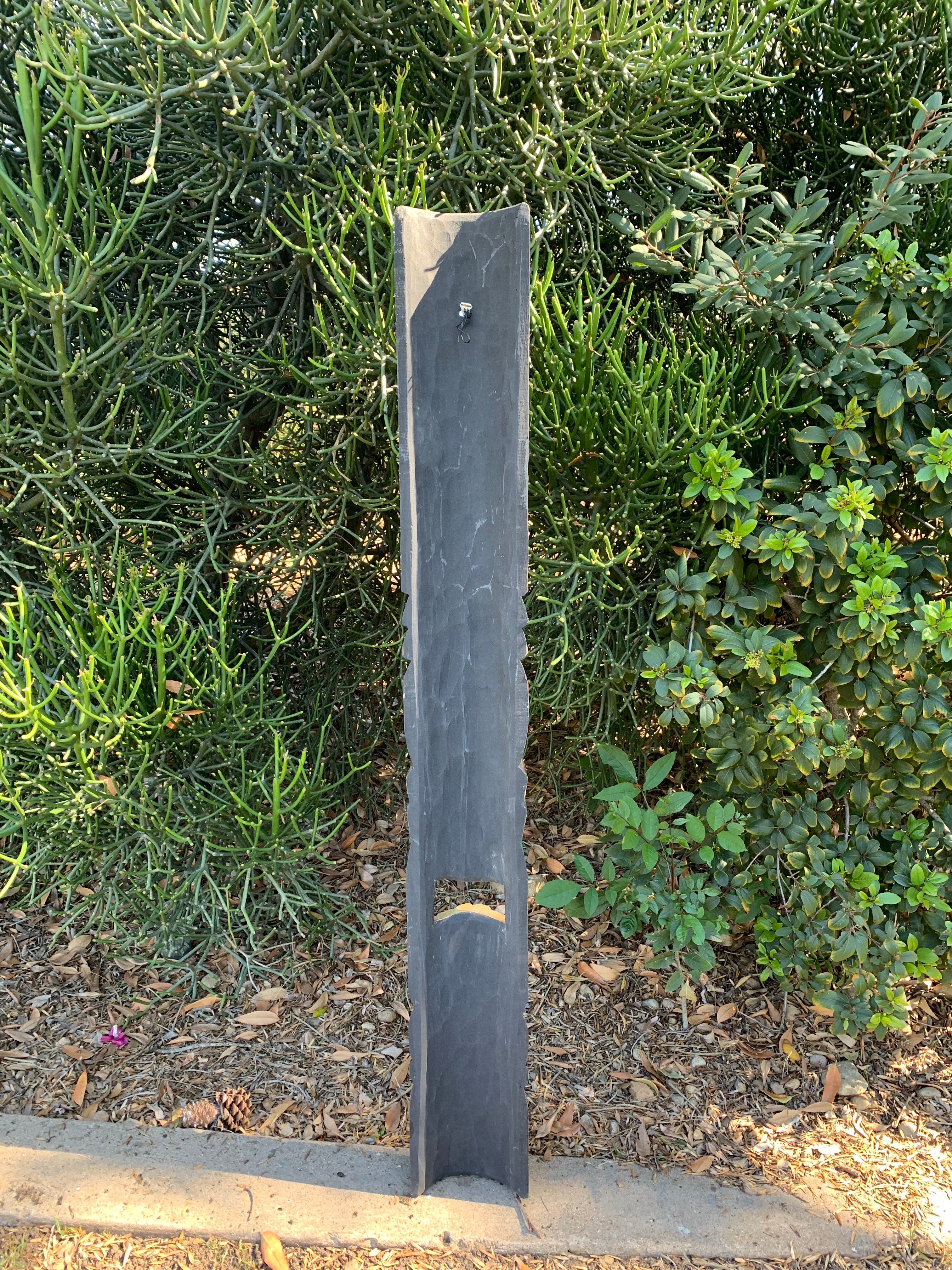 slate vertical post sculpture in a garden with dense green shrubs