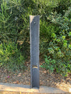 slate vertical post sculpture in a garden with dense green shrubs