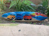Surfboard painted with yellow, blue, and red vintage Jeeps on a sandy beach at sunset