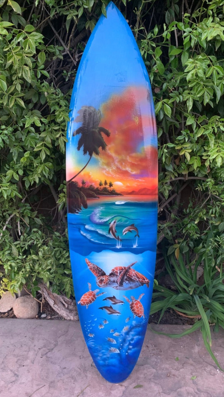 Colorful surfboard featuring a tropical sunset, palm trees, dolphins and turtles painted on it