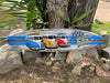 Colorful VW vans on a decorative surfboard with Welcome to Paradise text beside a tree