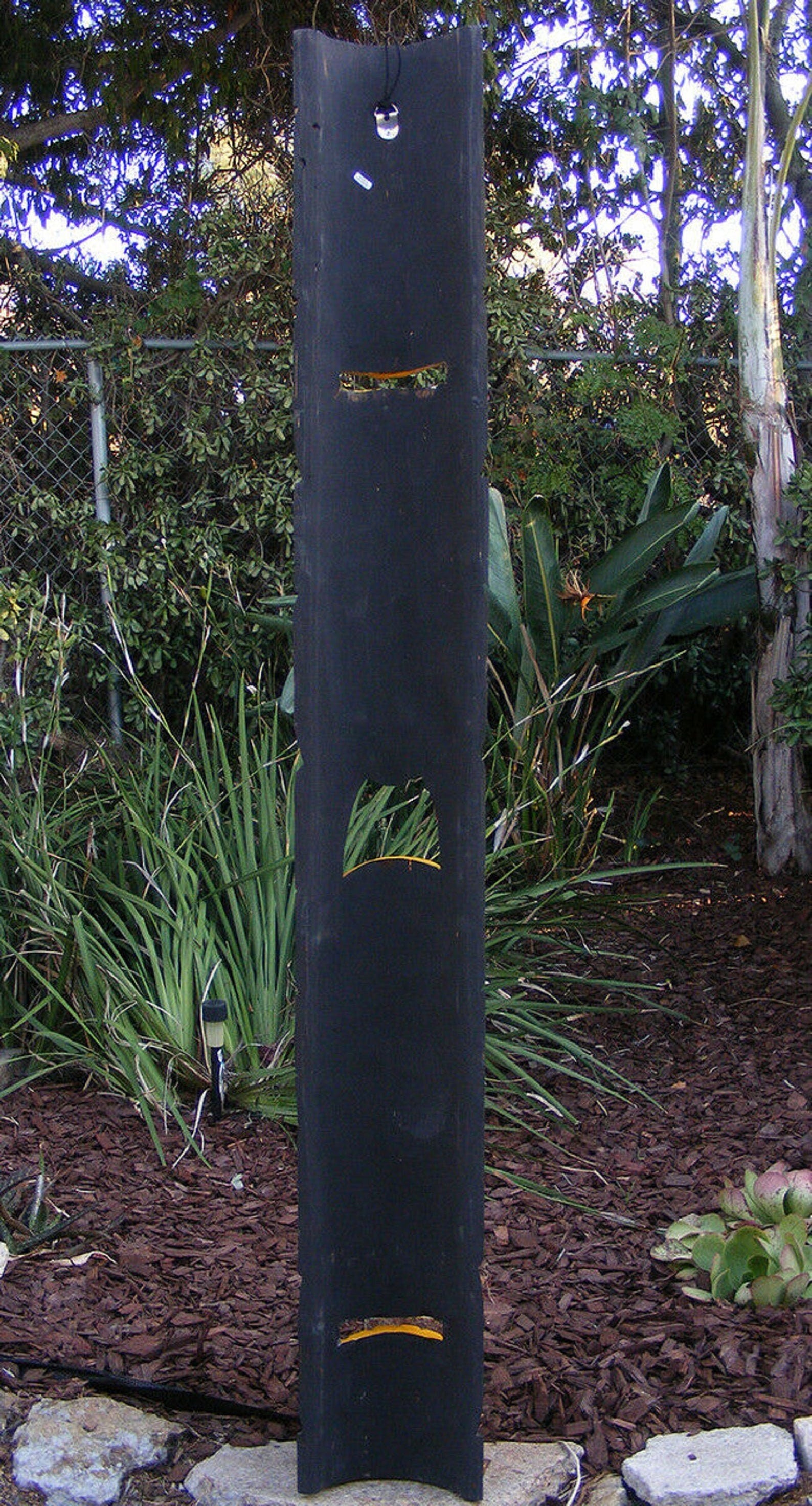 Tall black vertical post with curved cutouts in a landscaped garden