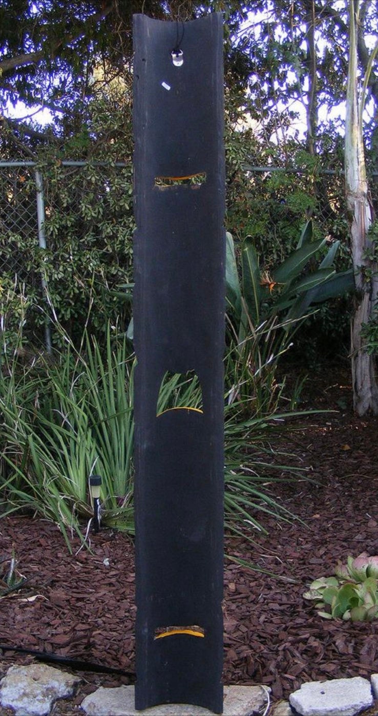 Tall black vertical garden sculpture with yellow-edged arched cutouts.