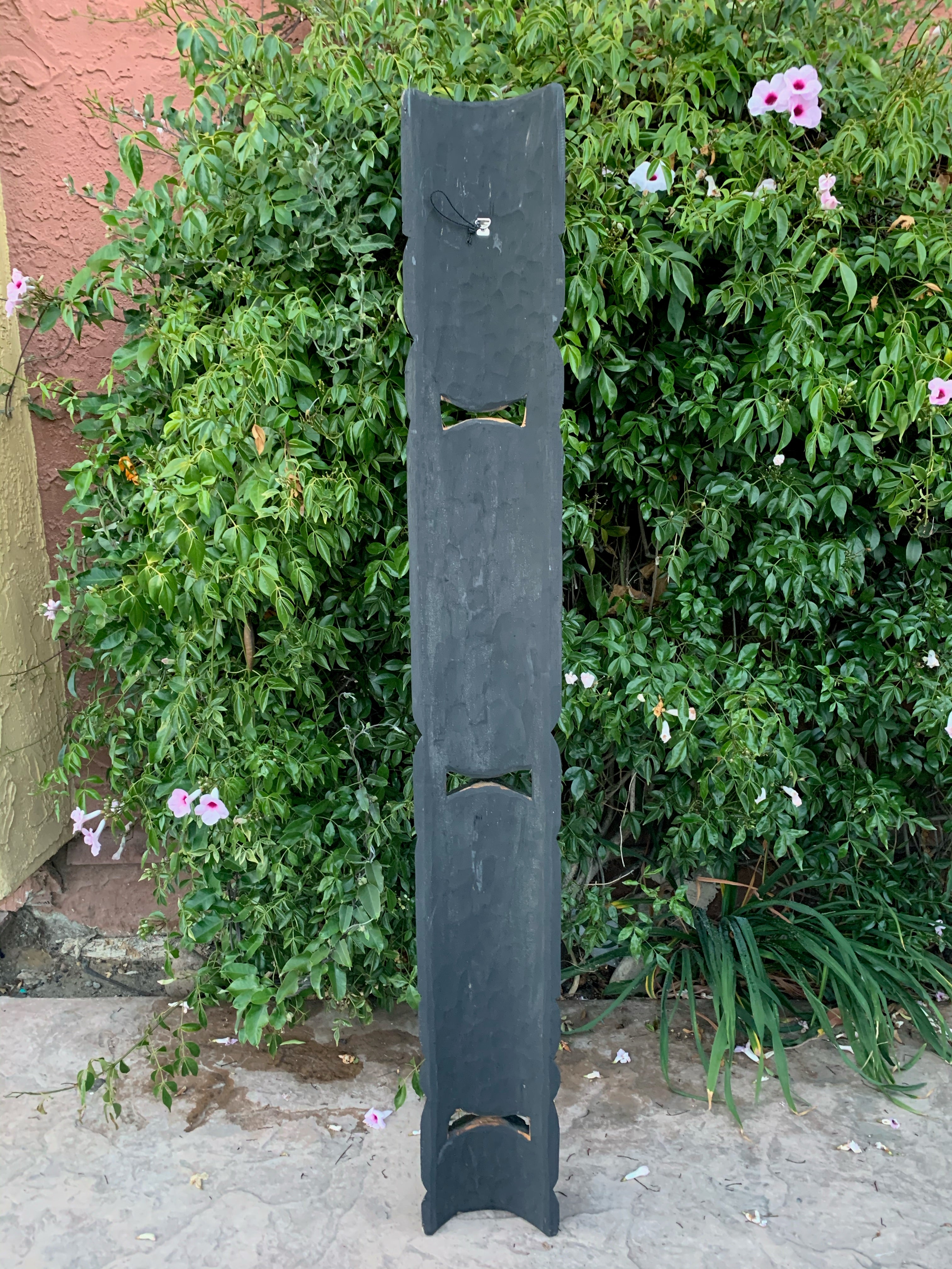 Tall vertical black metal sculpture with three arched cutouts in a garden