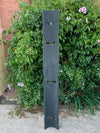 Tall vertical black metal sculpture with three arched cutouts in a garden