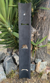tall black slate sculpture with cutouts leaning against a tree outdoors