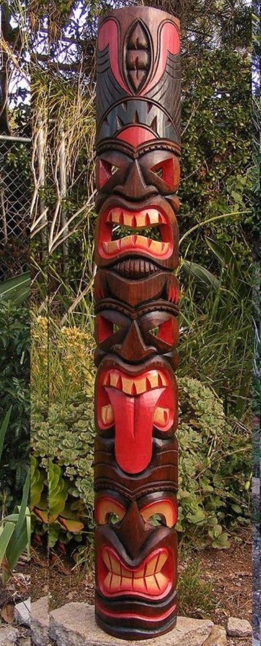 Tall carved tiki totem pole with red and brown faces outdoors