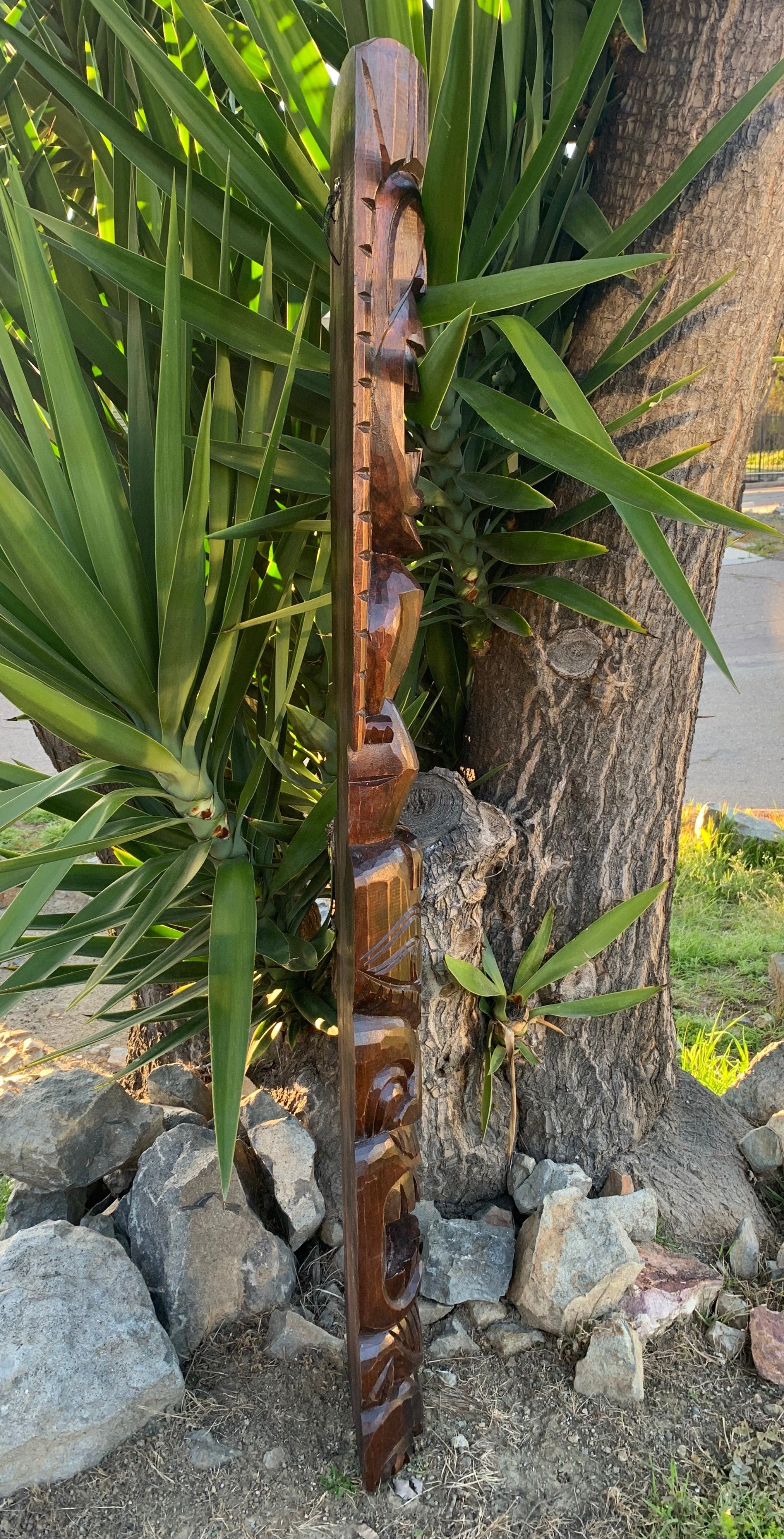 Tall wooden carved totem leaning against a tree among green tropical plants