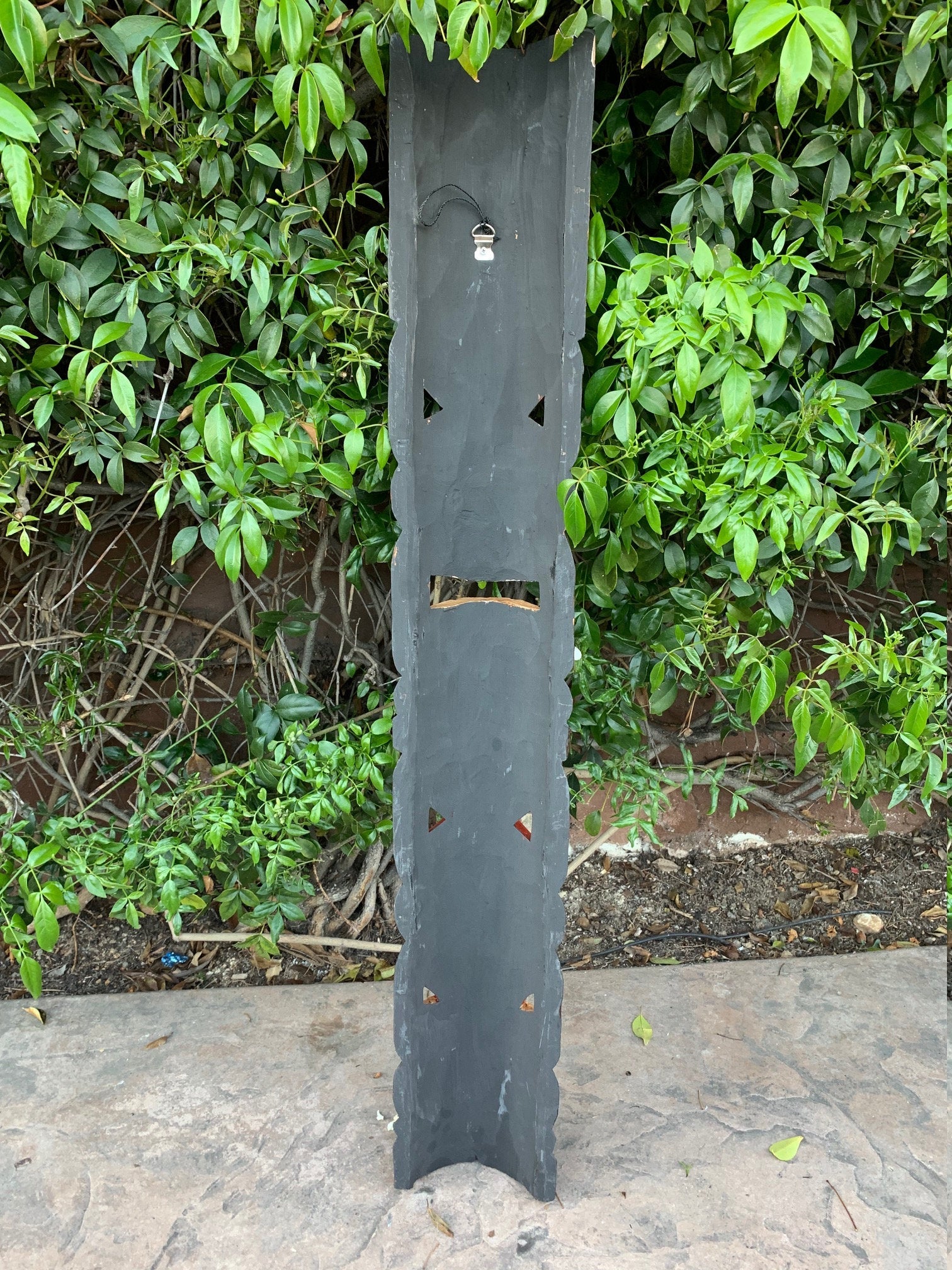 Tall dark-gray garden sculpture with triangular cutouts against lush green foliage