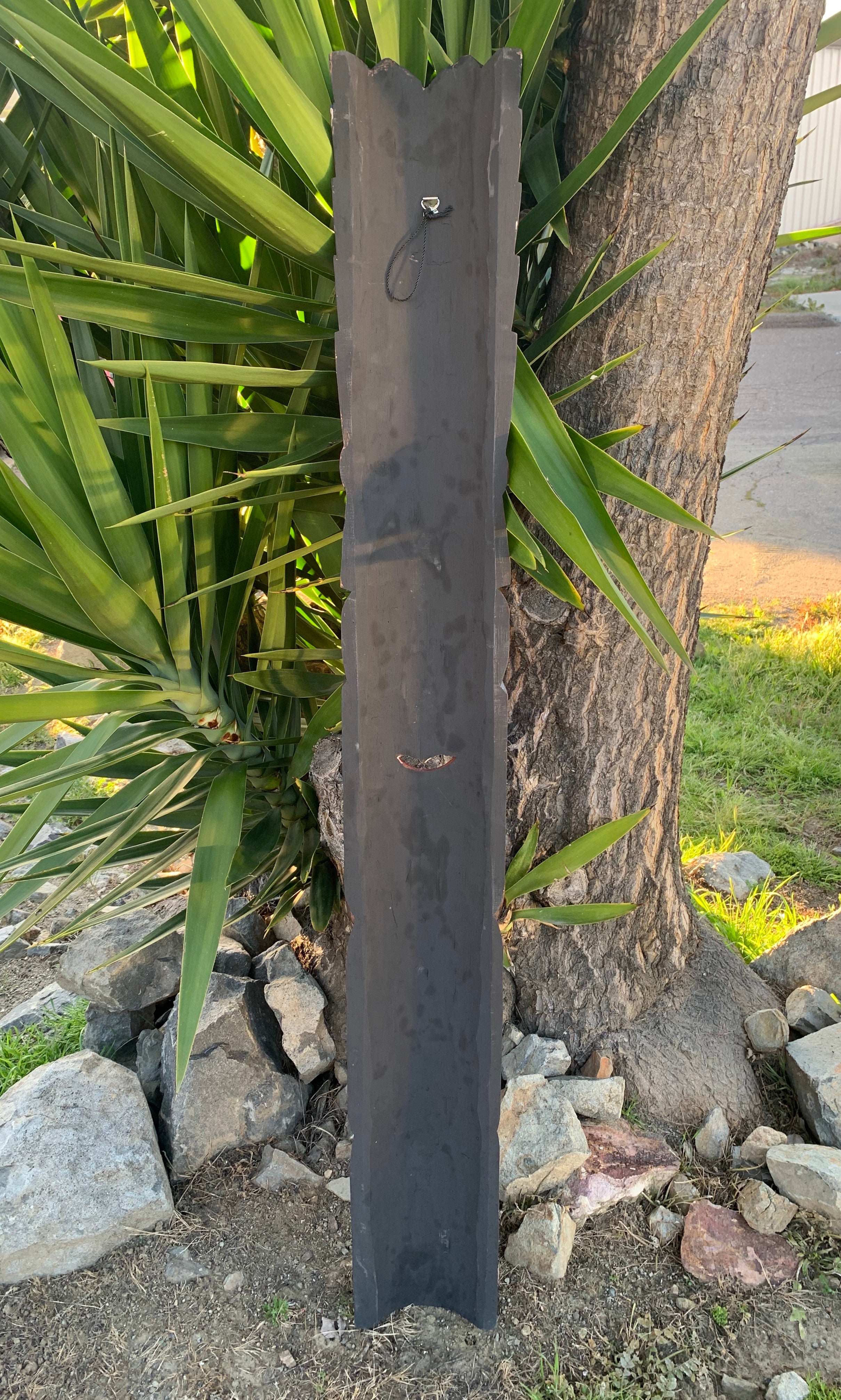 Tall dark slate post with jagged top beside a tree in a garden