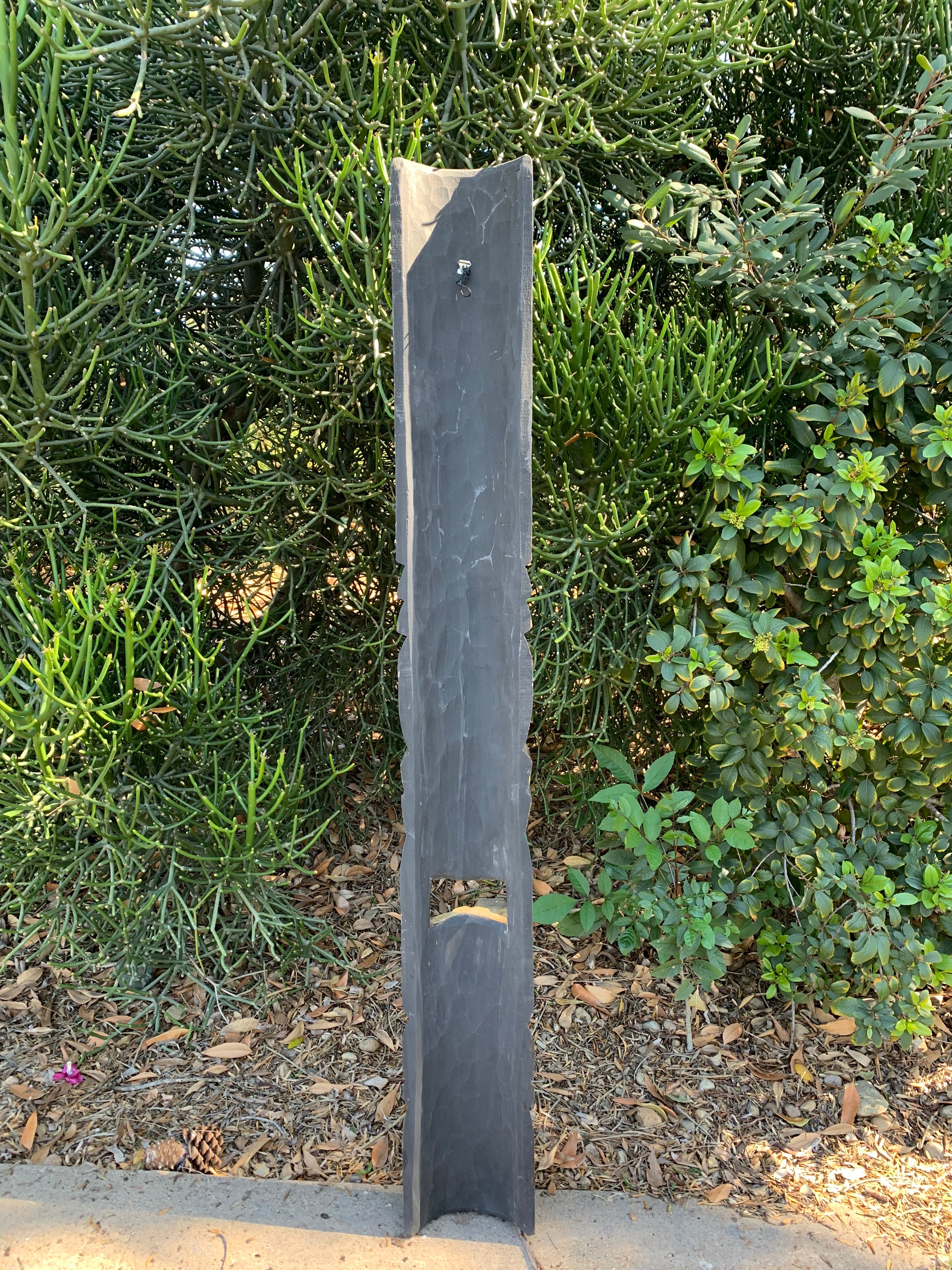 Tall dark slate post with a notch in a garden setting.