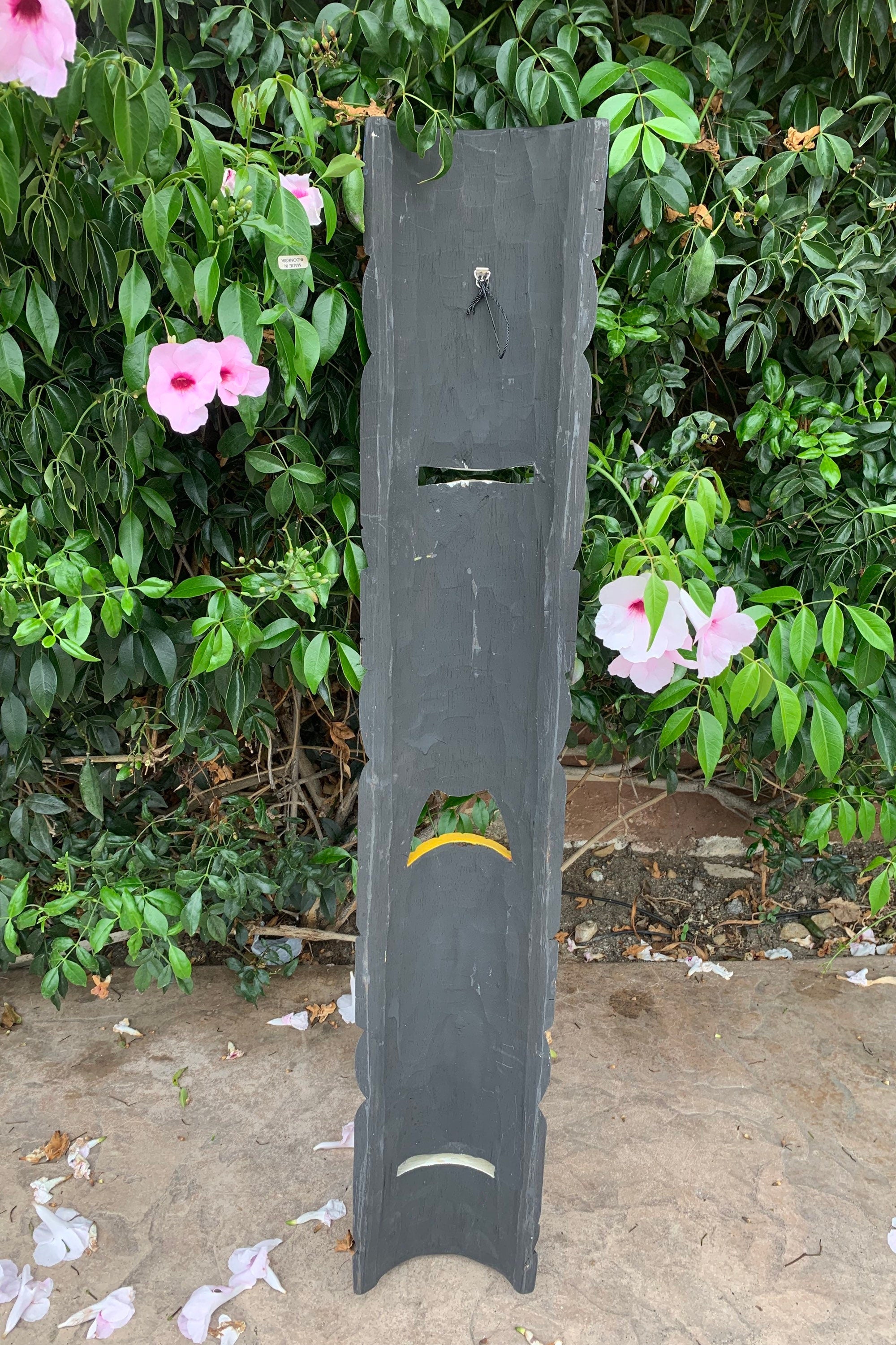 Tall dark weathered wooden post with a mail slot and curved cutouts in a garden setting