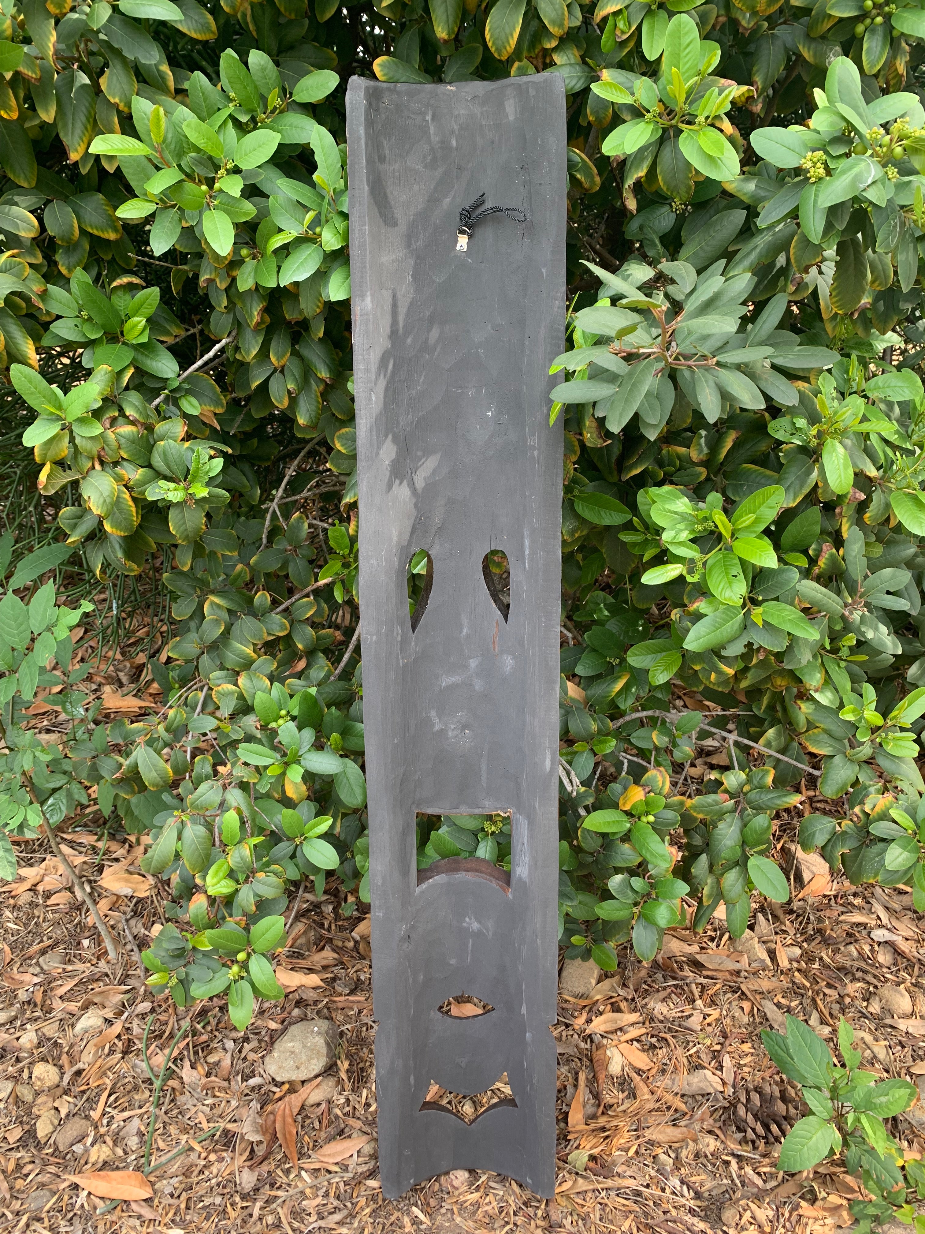 tall-gray-wooden-post-with-teardrop-cutouts-in-greenery