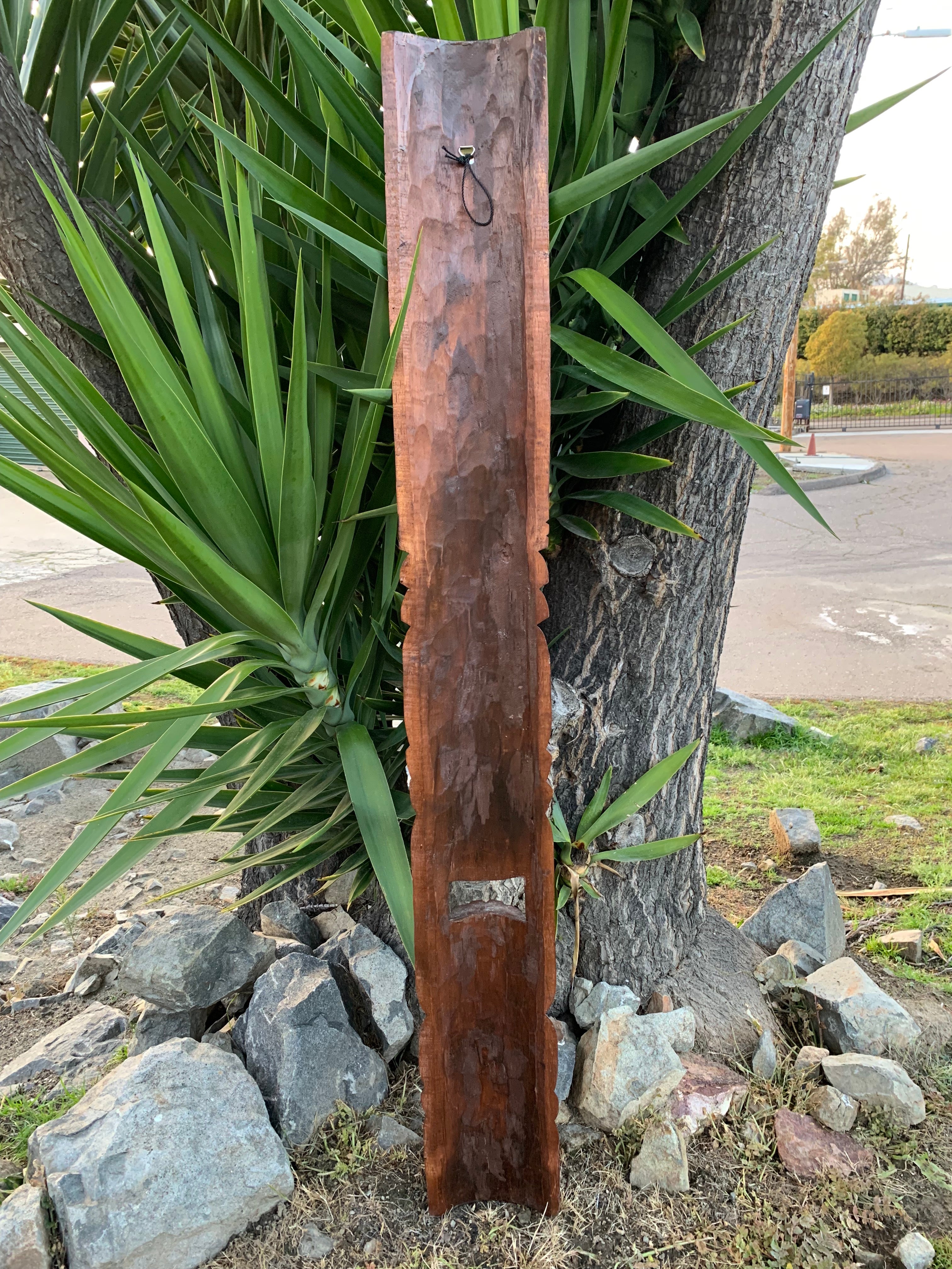 Tall narrow wooden panel leaning against a tree in a garden with rocks and green plants