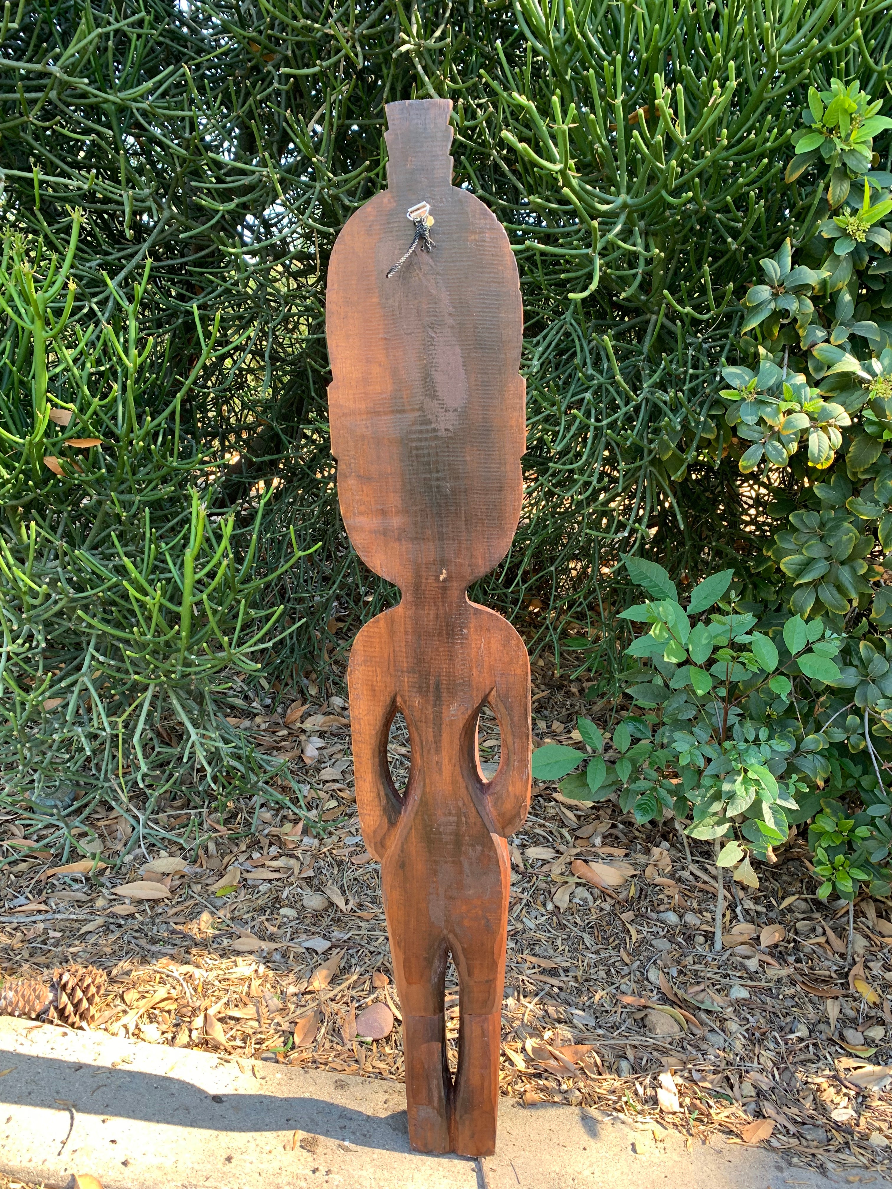 tall rustic wooden carved human silhouette statue with hollow arm openings outdoors