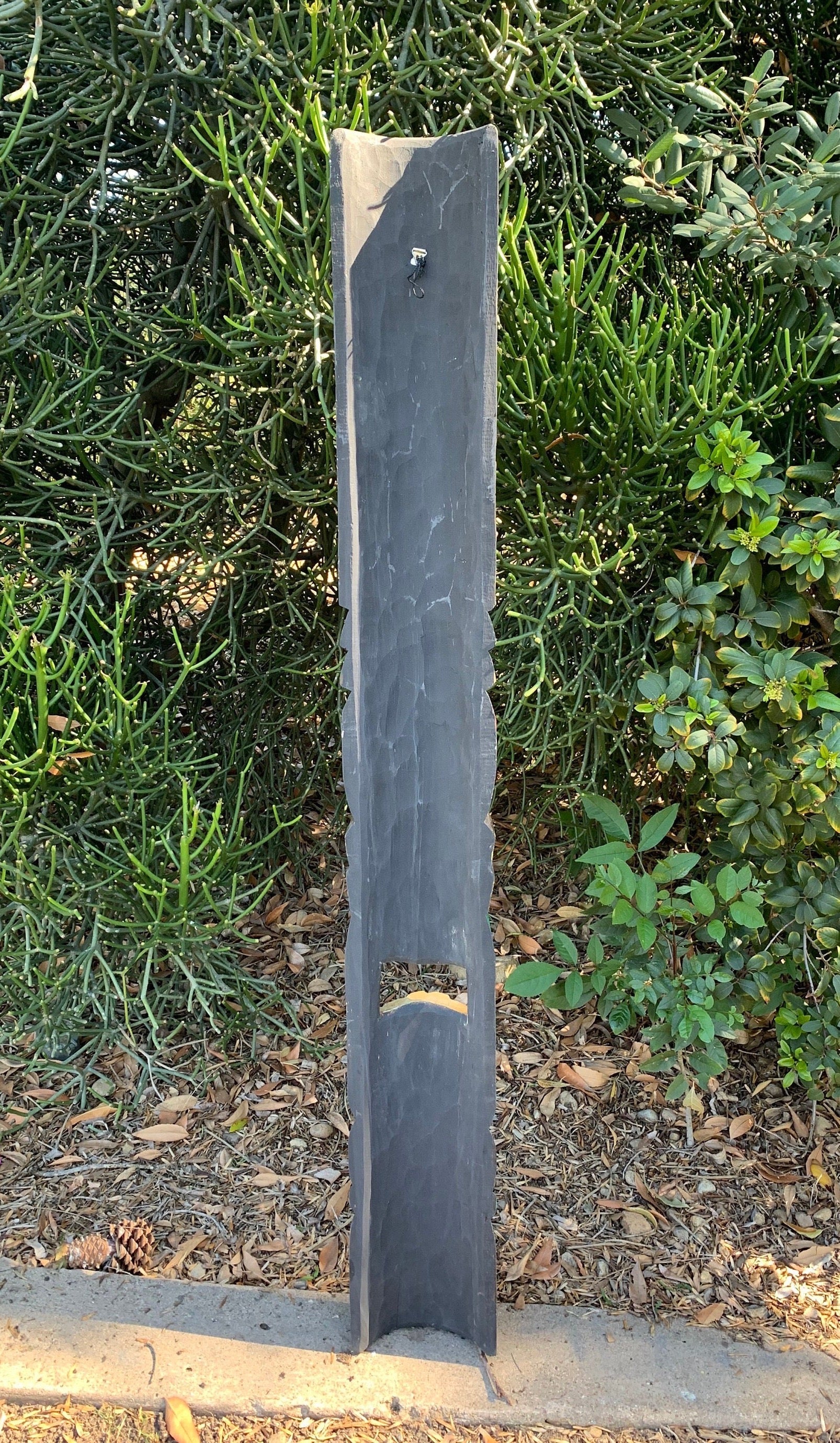 Tall slate garden post with a small metal hook in front of dense succulents.