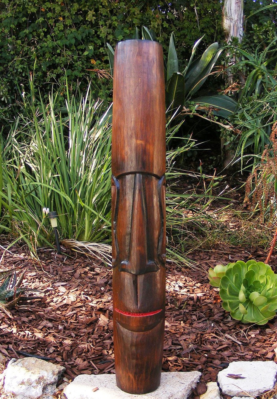 tall wooden tiki statue with carved face in garden