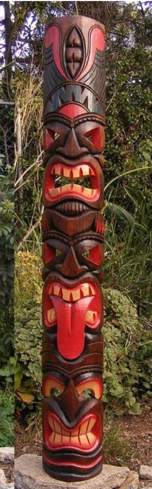 Tall wooden tiki totem pole with stacked carved faces in a garden