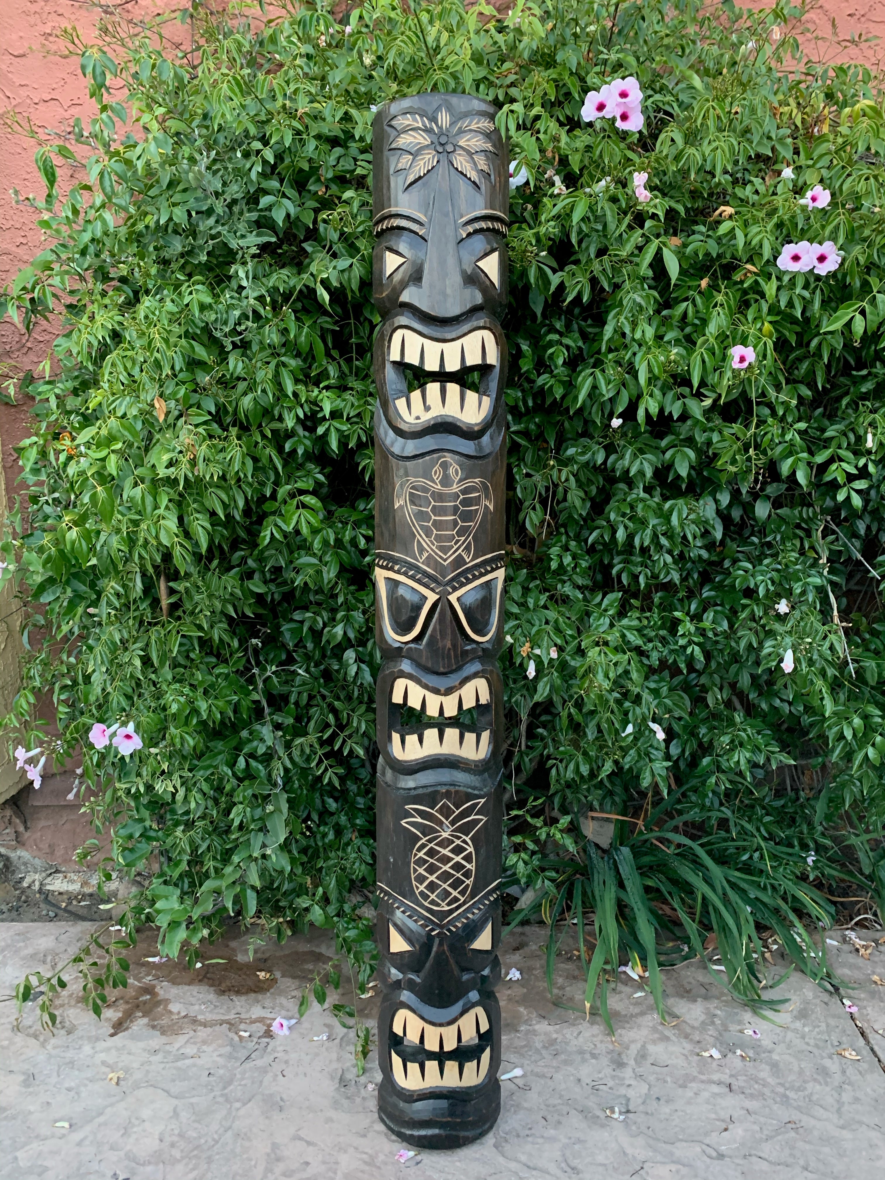Tall wooden totem pole with multiple carved faces in a garden setting