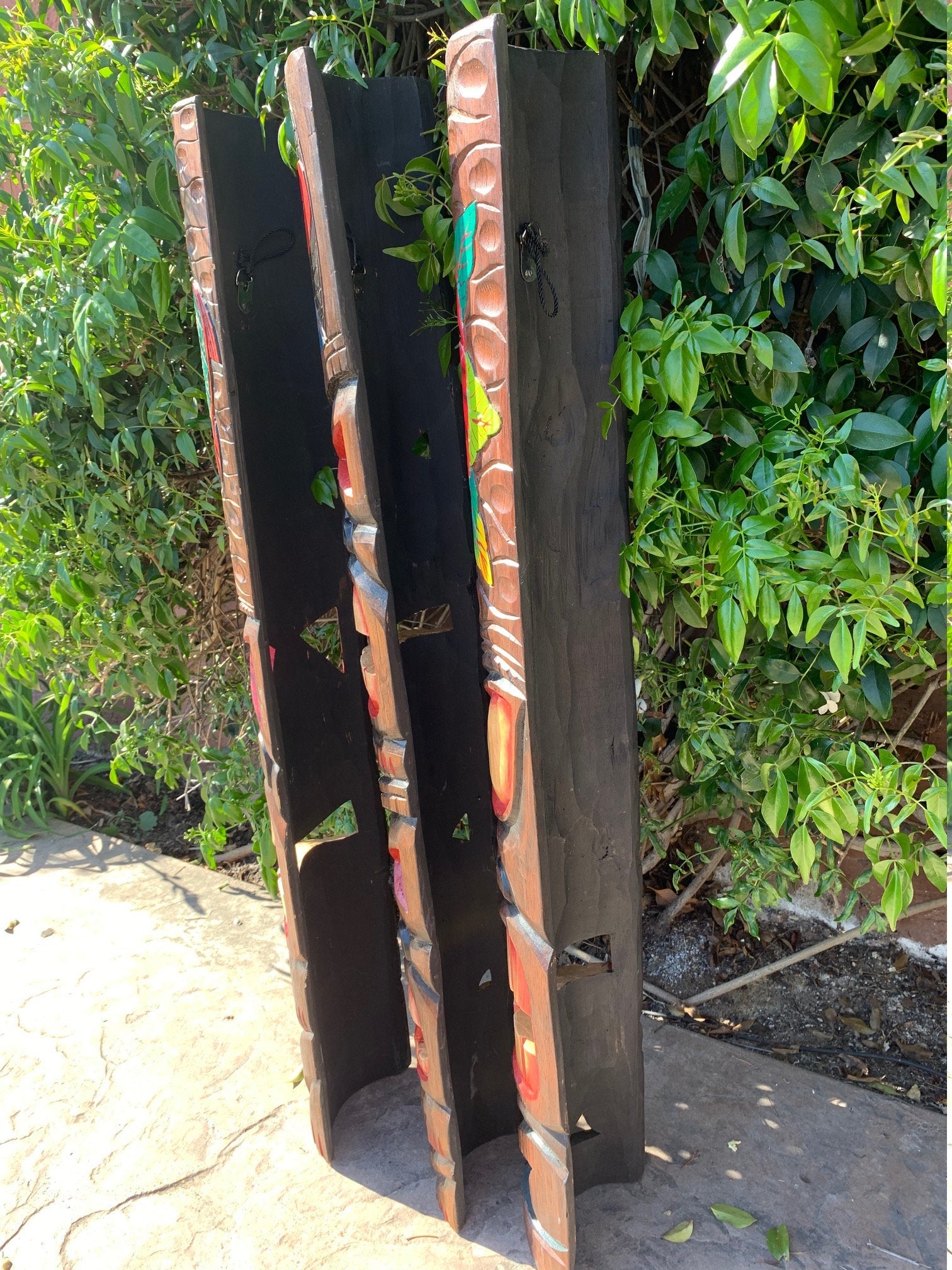 Three tall carved wooden panels with geometric patterns leaning against a green hedge outdoors.