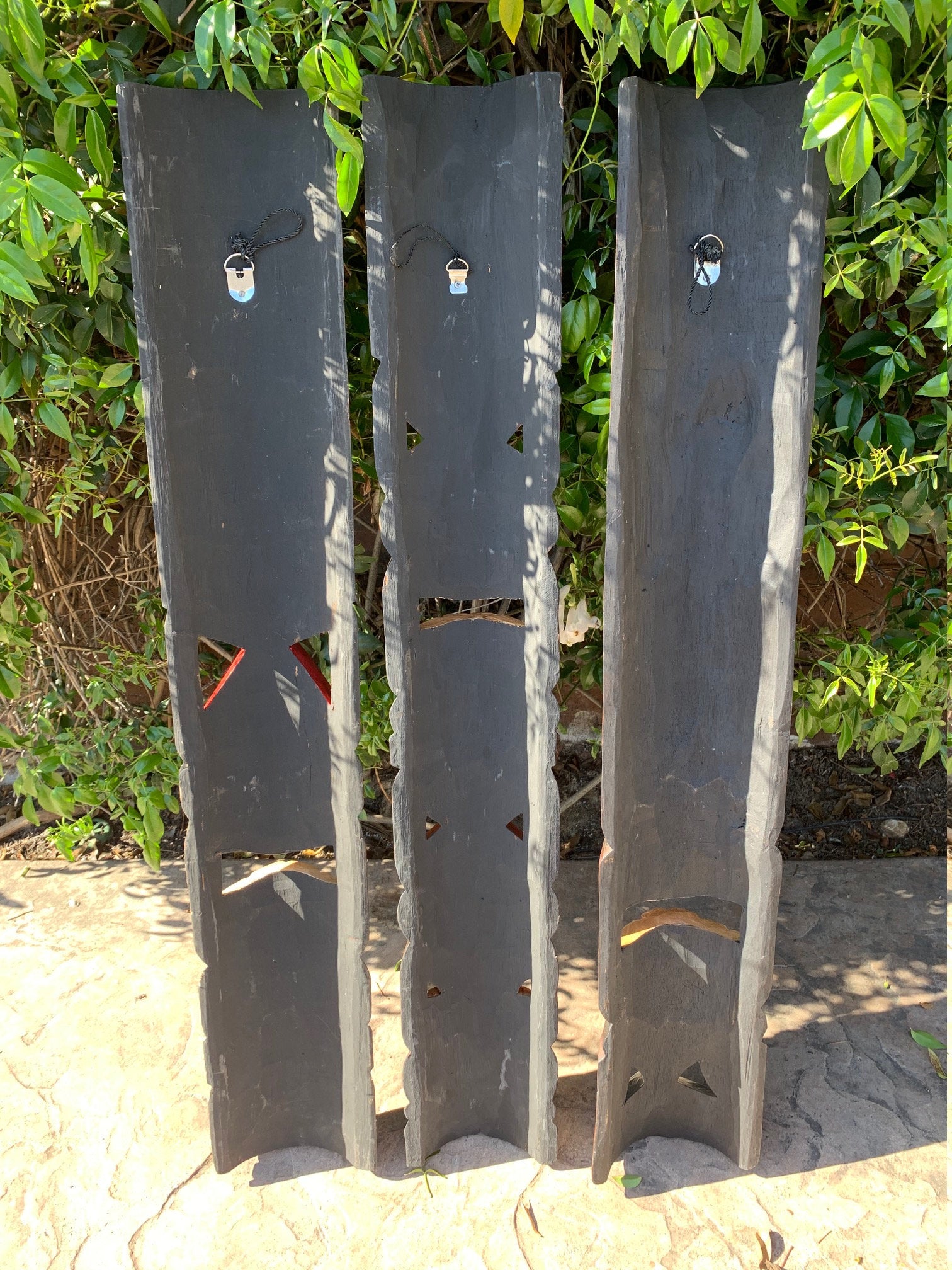 Three tall slate garden screens with triangular and rectangular cutouts standing outdoors by a green hedge.