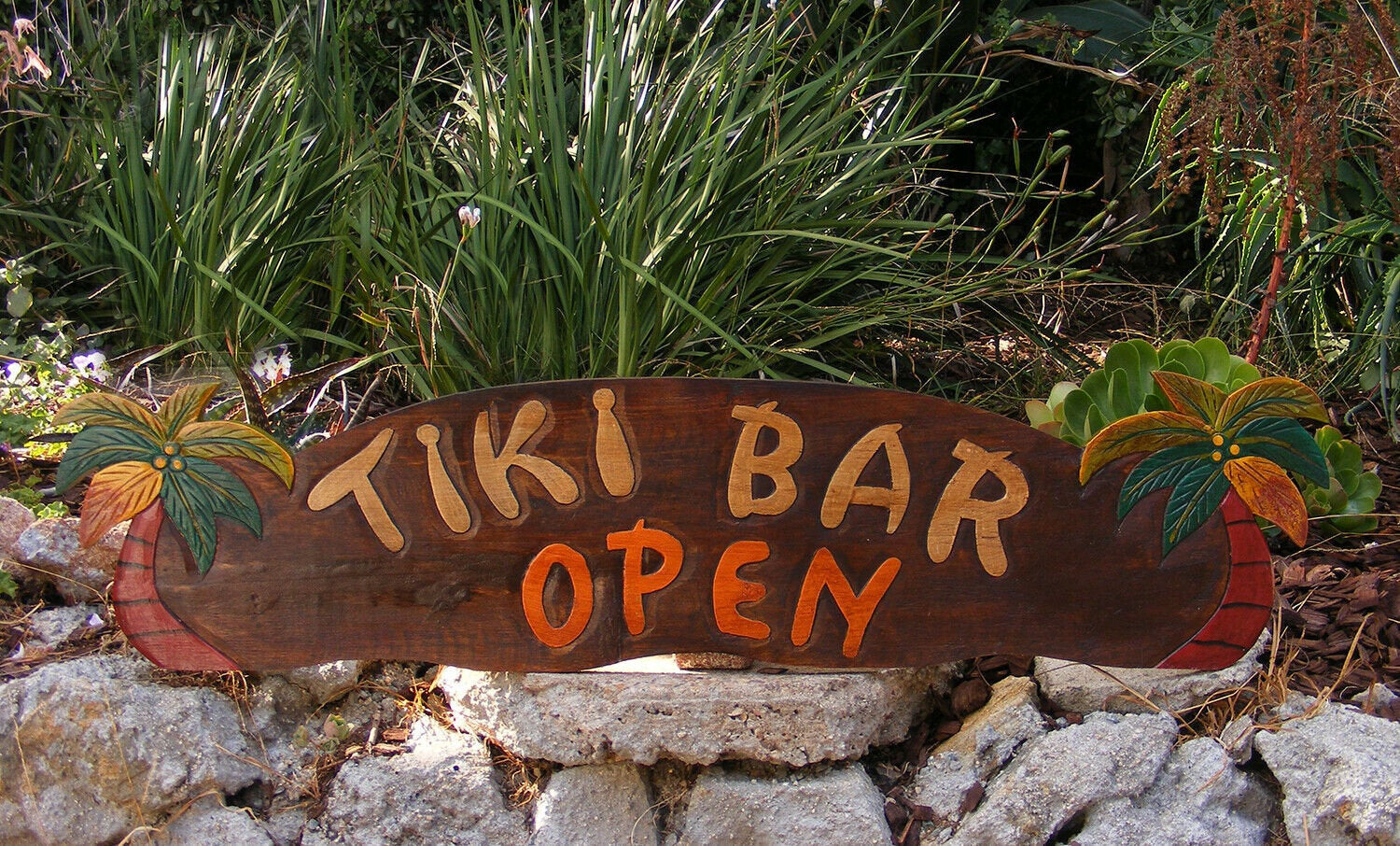 Wooden tiki bar open sign with palm trees in a garden