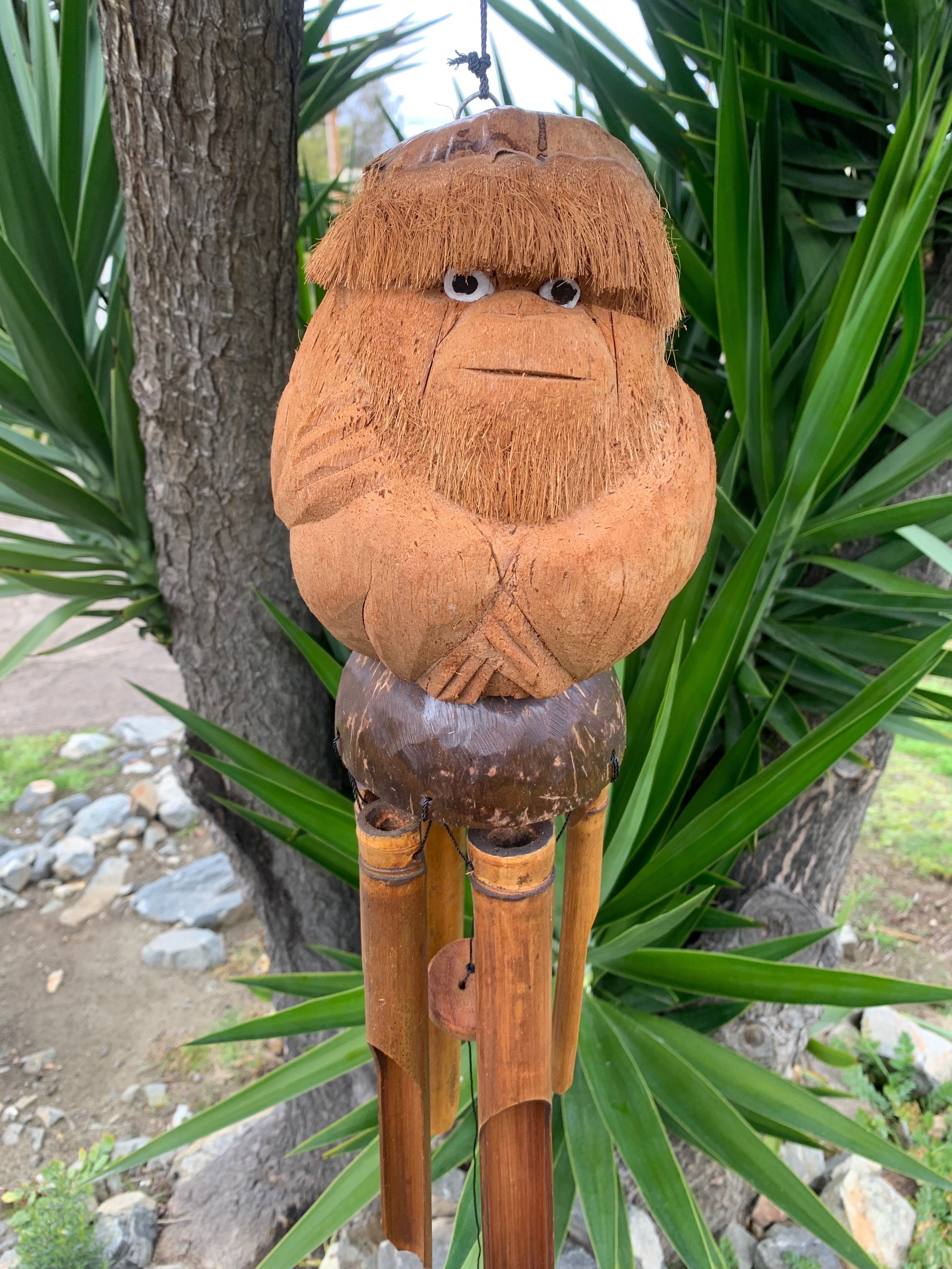 Carved coconut tiki statue with straw hair and bamboo legs outdoors