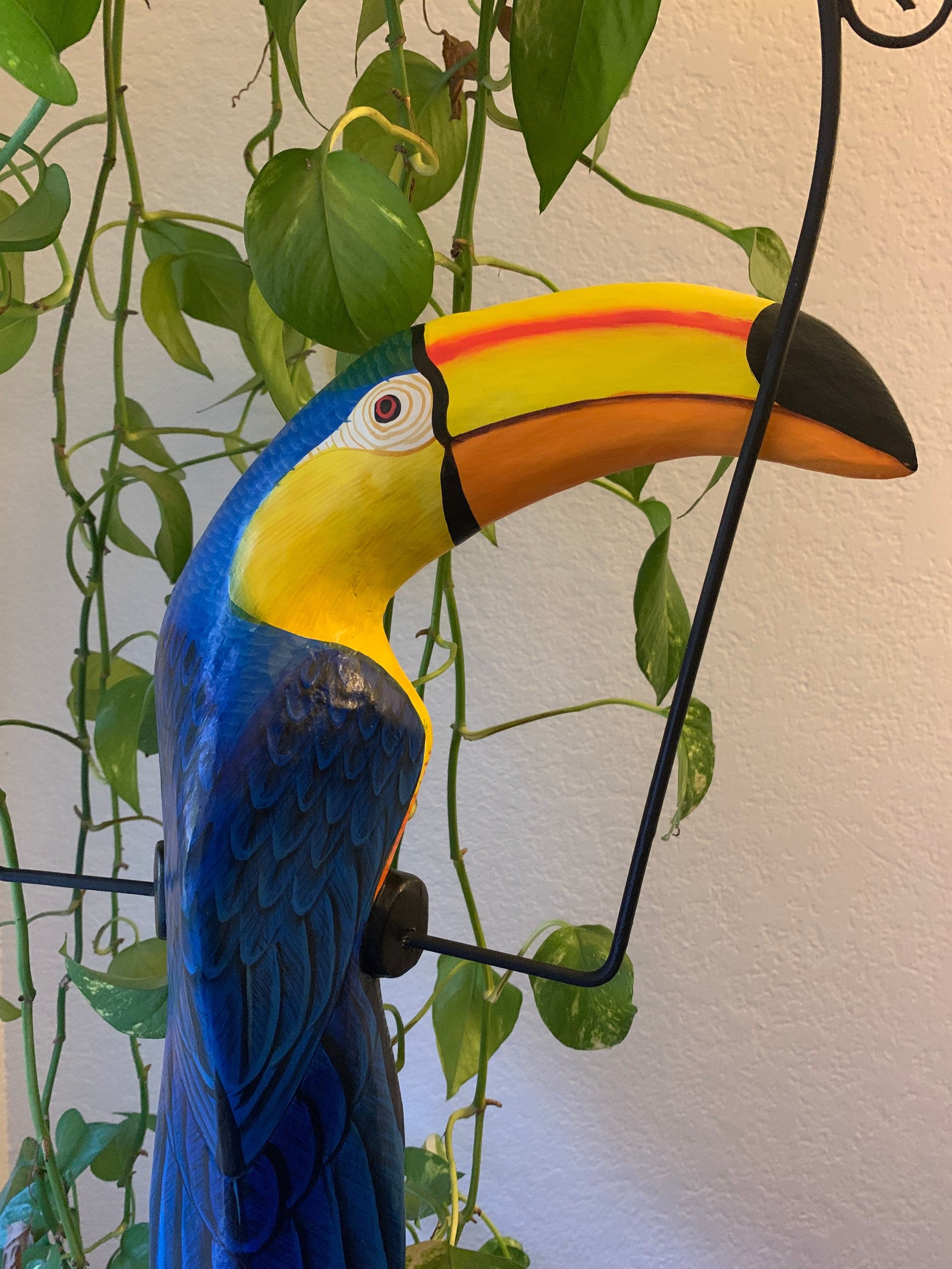 Vibrant painted toucan sculpture with bright blue body and multicolor beak among trailing green plants