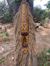 Intricately carved tribal wooden mask with gold swirls hanging on a tree trunk with fiber fringe