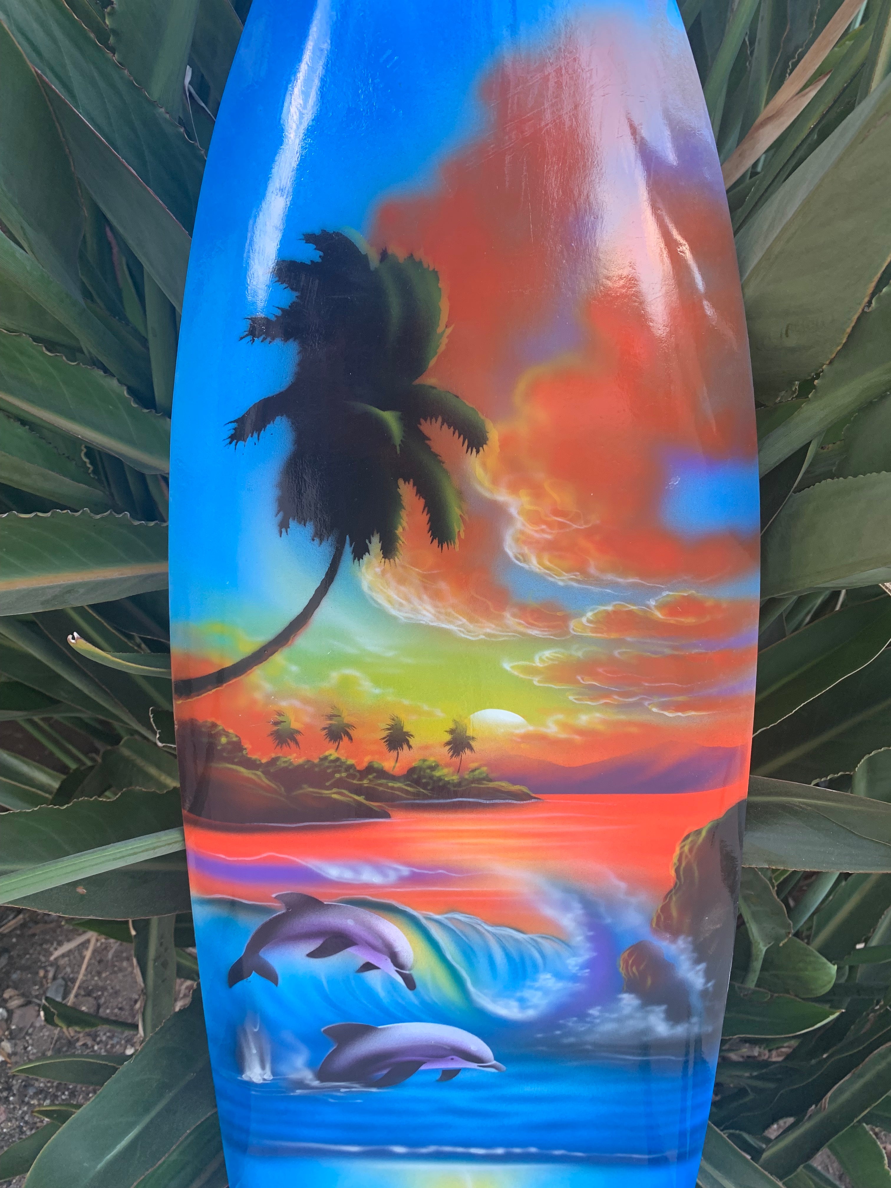 Painted surfboard featuring a tropical sunset, palm trees, and playful dolphins in the ocean