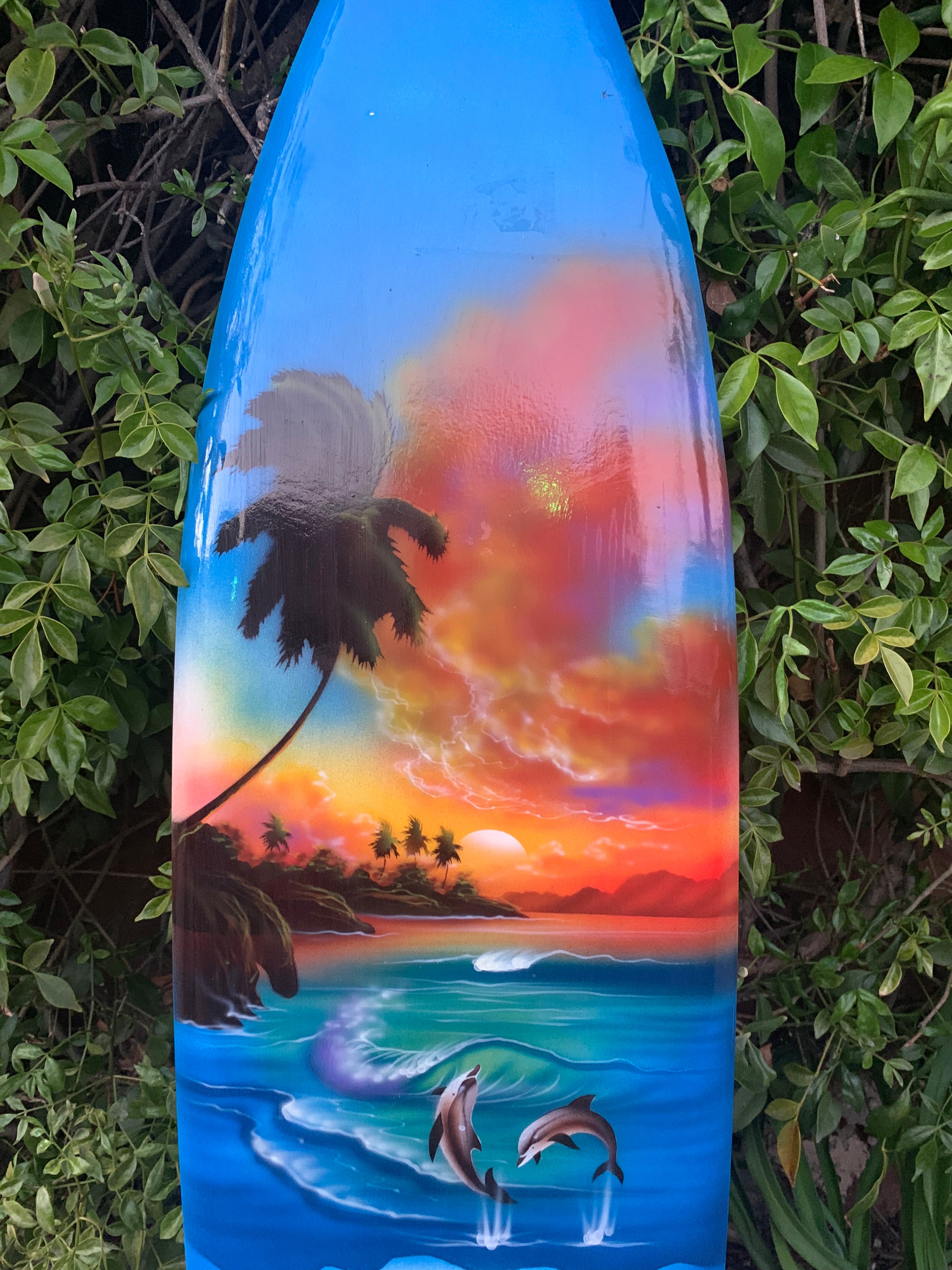 Vibrant tropical sunset painted on a blue surfboard with palm trees and dolphins.