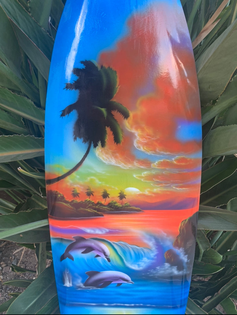Colorful tropical sunset surfboard art with palm trees, an island, and dolphins.