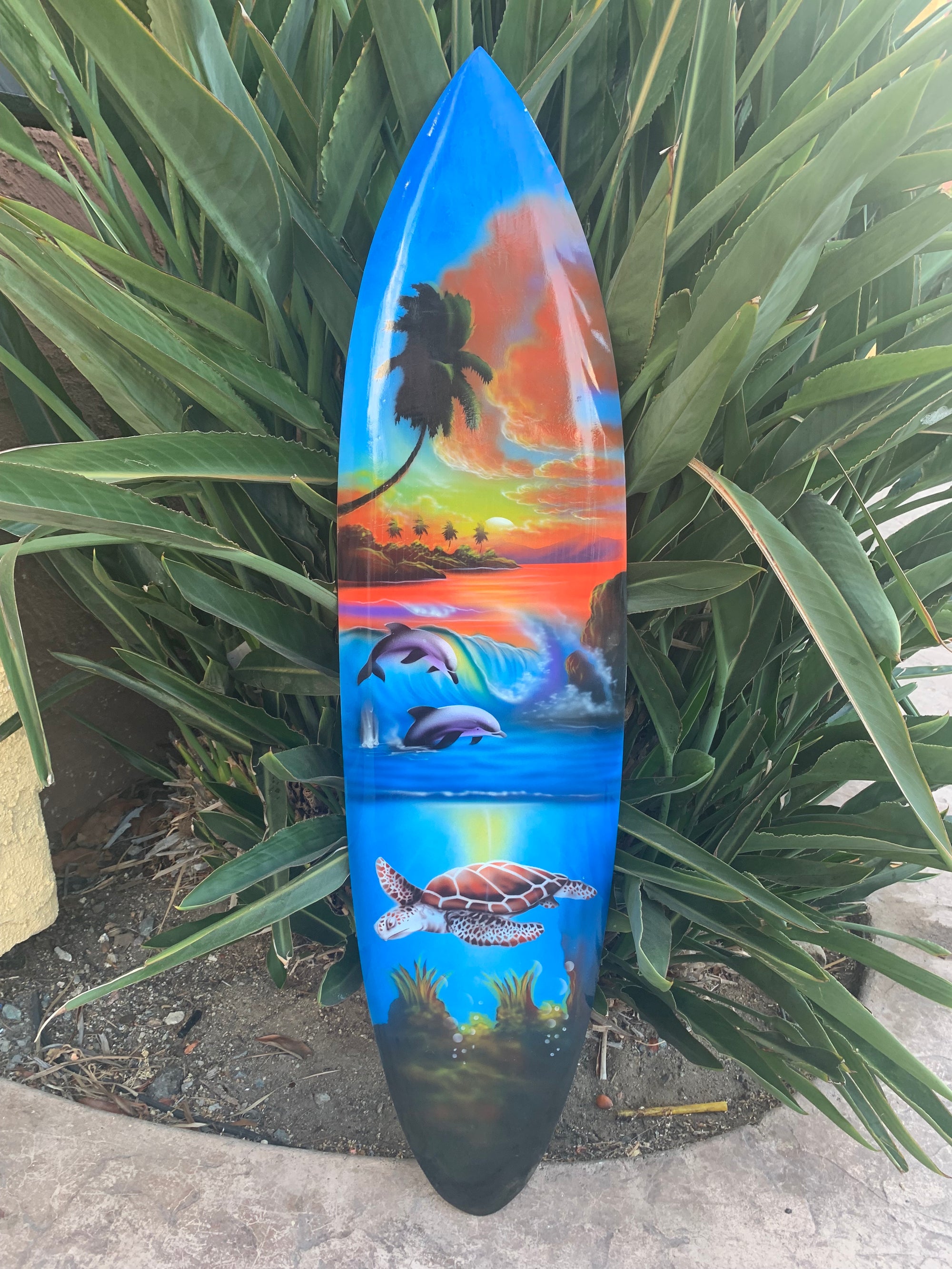 Colorful surfboard painting of a tropical sunset, palm trees, dolphins, and a sea turtle.
