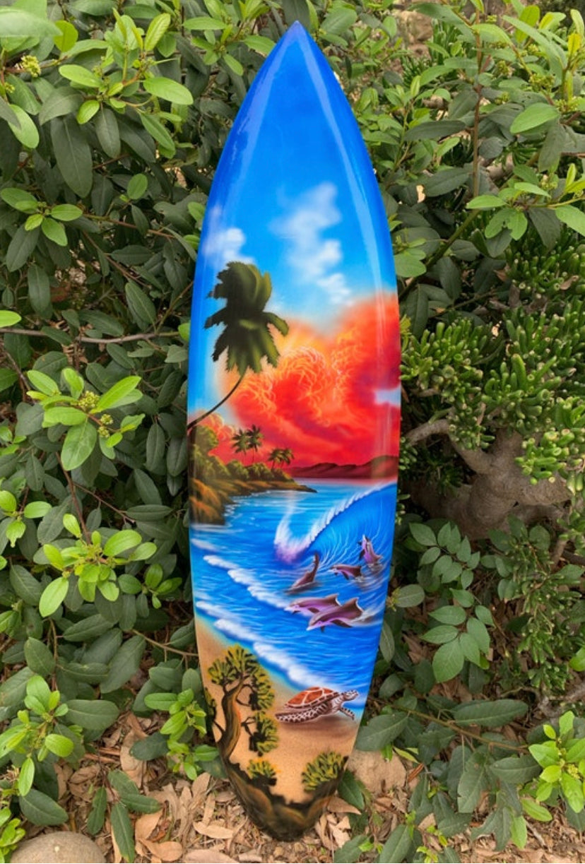 Colorful painted surfboard with tropical beach scene, palm trees, sunset, dolphins, waves, and a sea turtle.