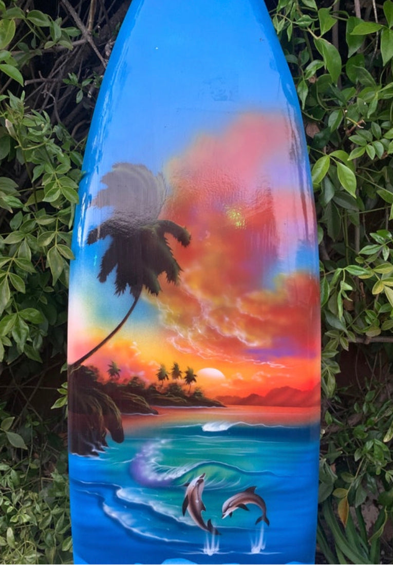 Colorful tropical sunset on a blue surfboard with palm trees and jumping dolphins.