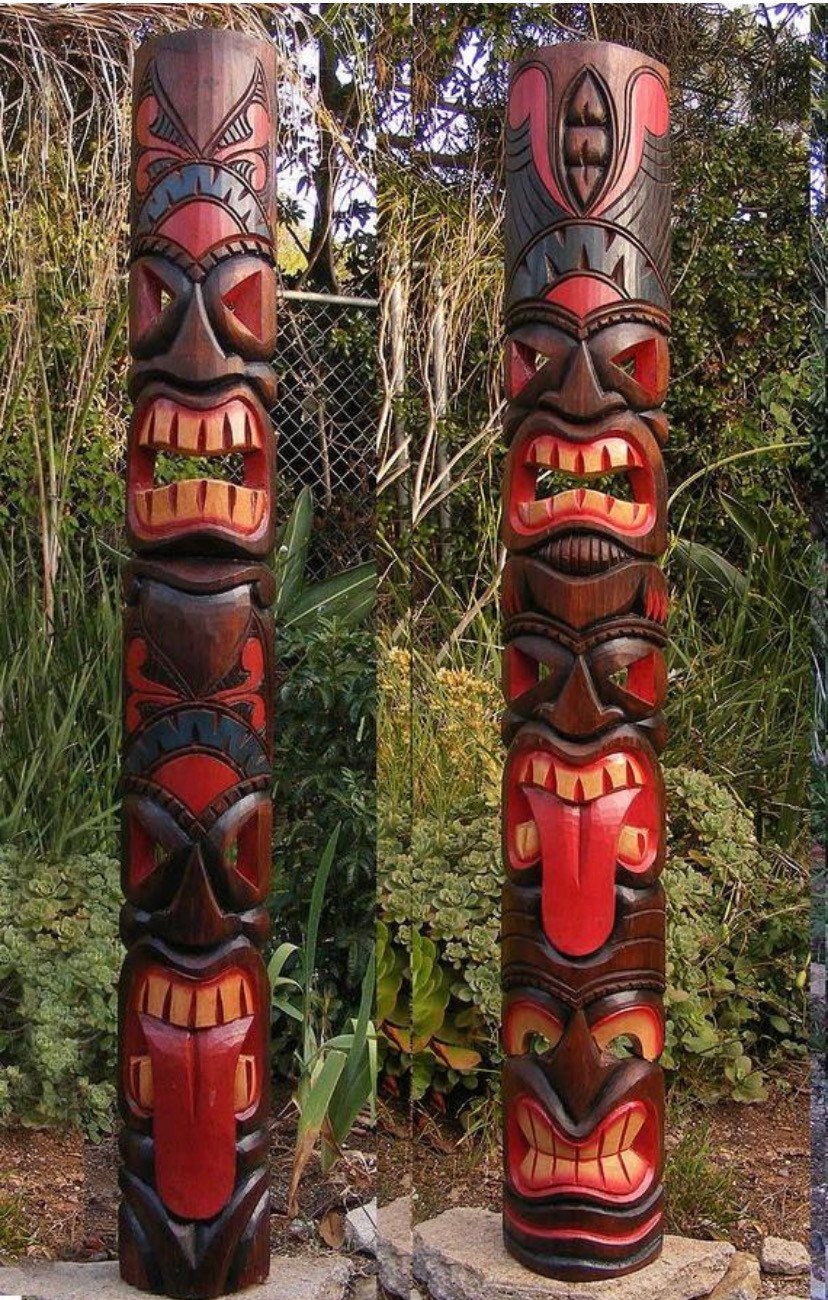 Two carved wooden totem poles with red and yellow facial features in a garden setting