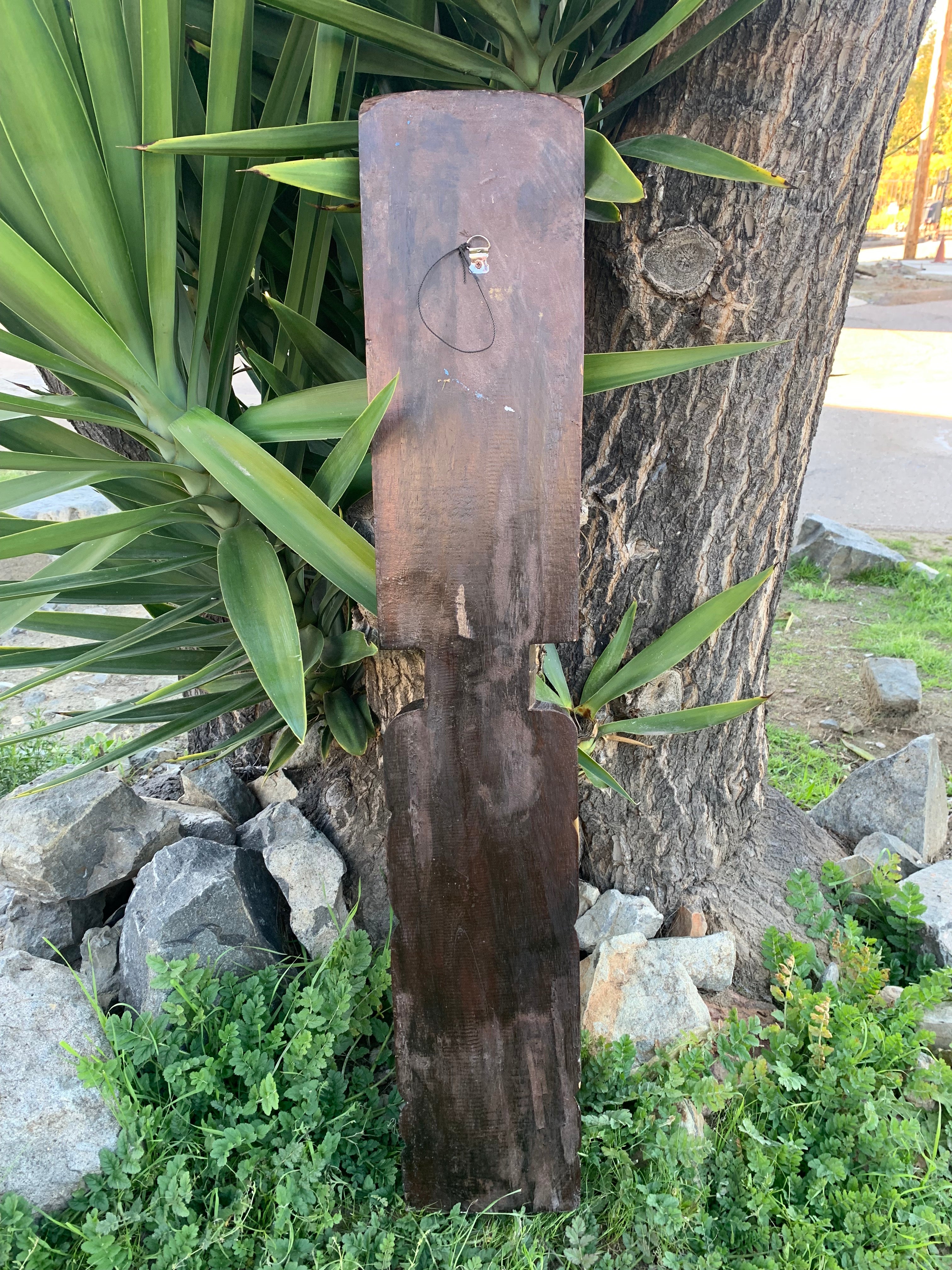 Weathered wooden signboard mounted on a tree trunk among green plants