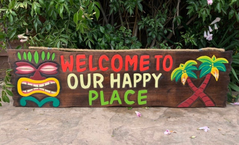 Colorful wooden sign reading Welcome to Our Happy Place with a tiki mask and palm trees