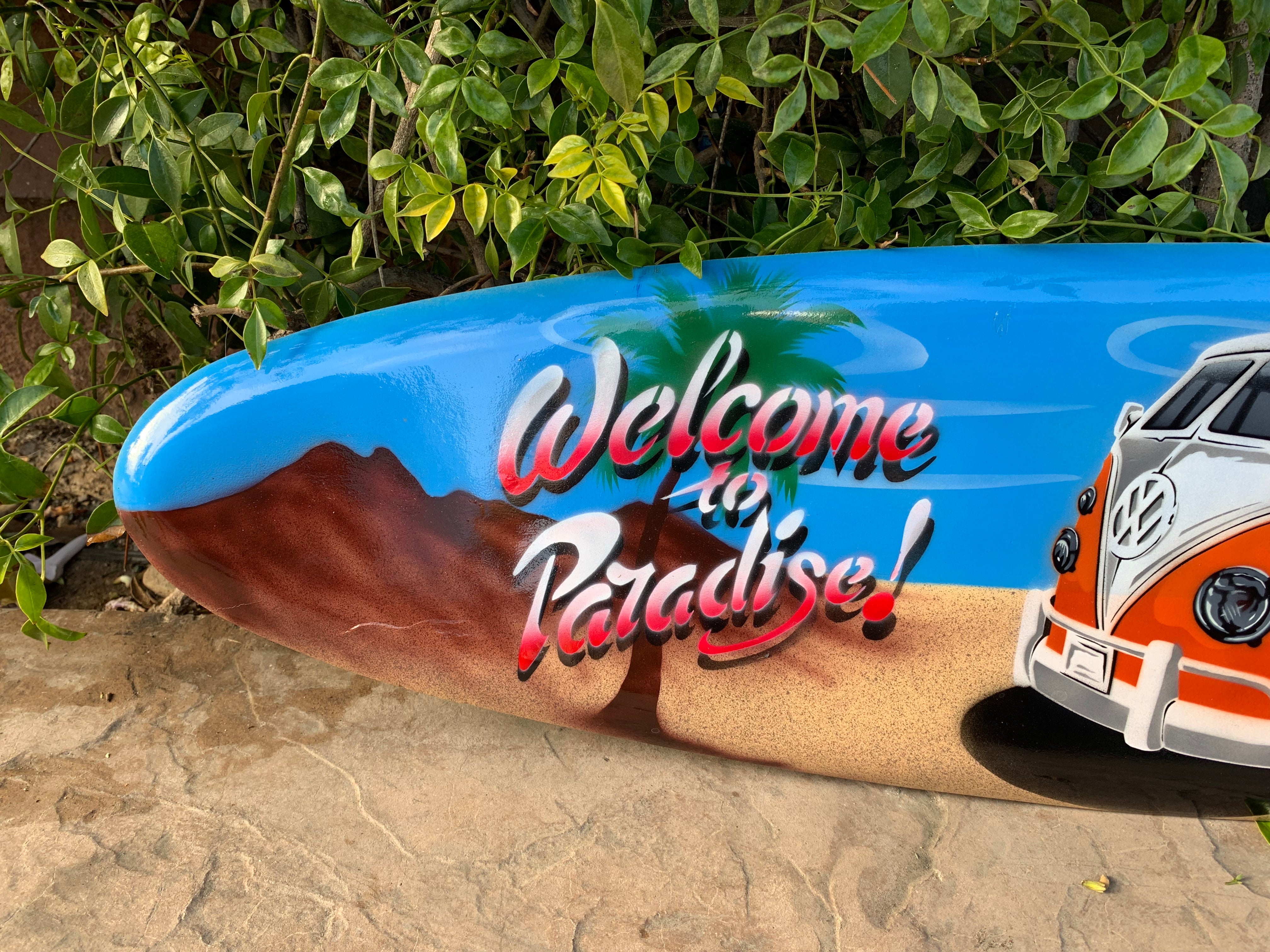 Bright blue surfboard mural with 'Welcome to Paradise' text, palm trees, sandy beach, and a vintage VW van.