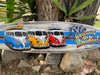 Colorful surfboard sign featuring four Volkswagen vans in blue, yellow, orange and red with the text Welcome to Paradise.