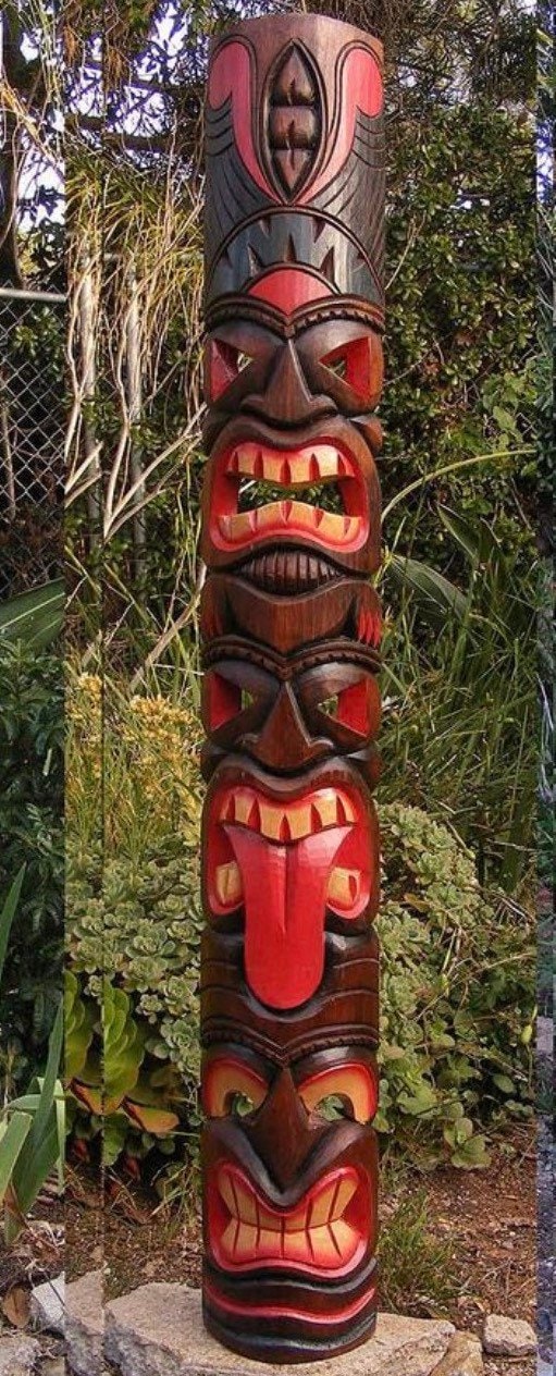 carved wooden totem pole with stacked faces in red and brown, outdoors