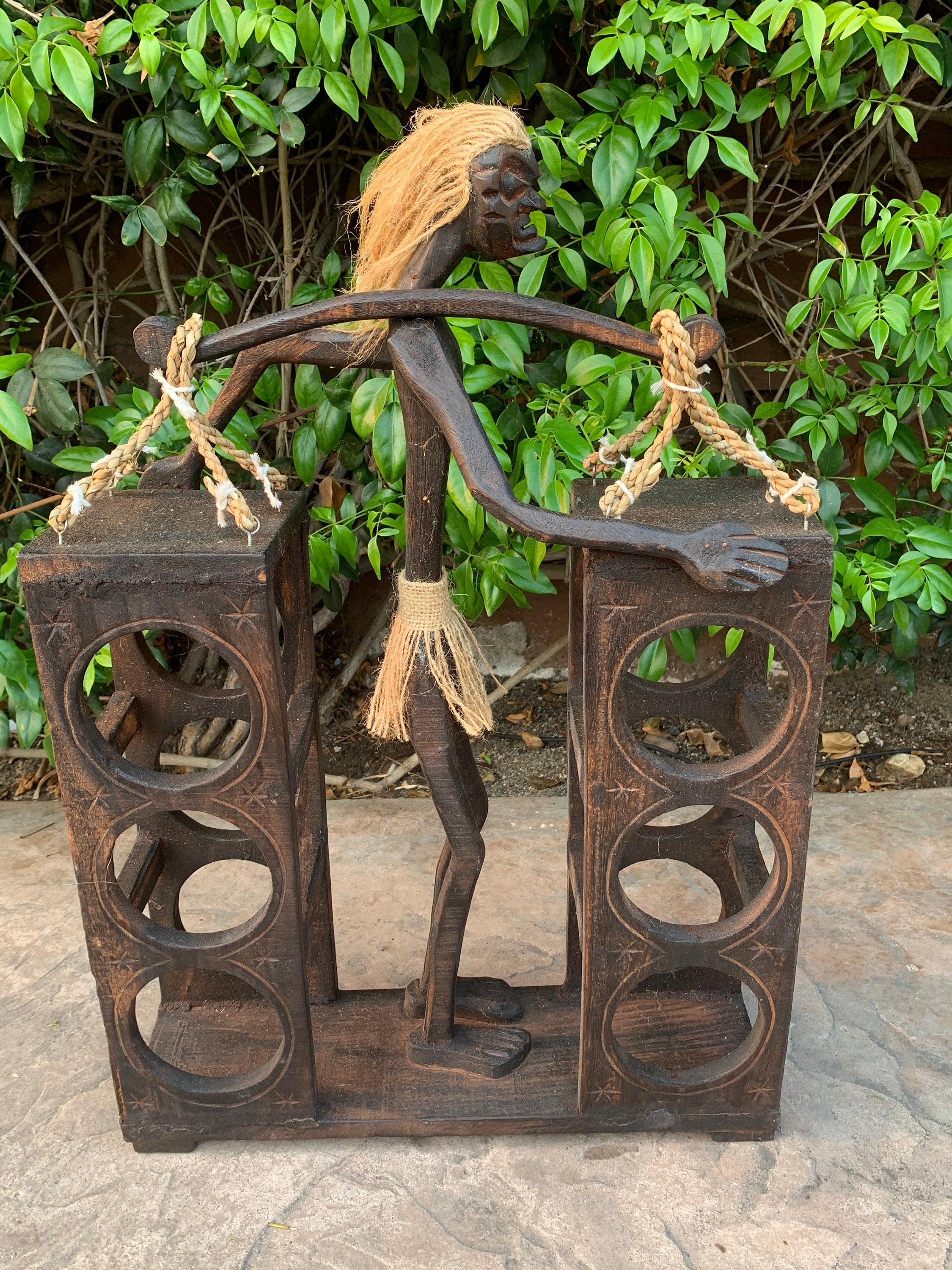 wooden carved humanoid figure between two circular-holed stands with rope handles