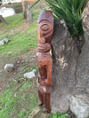 Wooden carved tiki totem statue leaning against a tree in a garden.