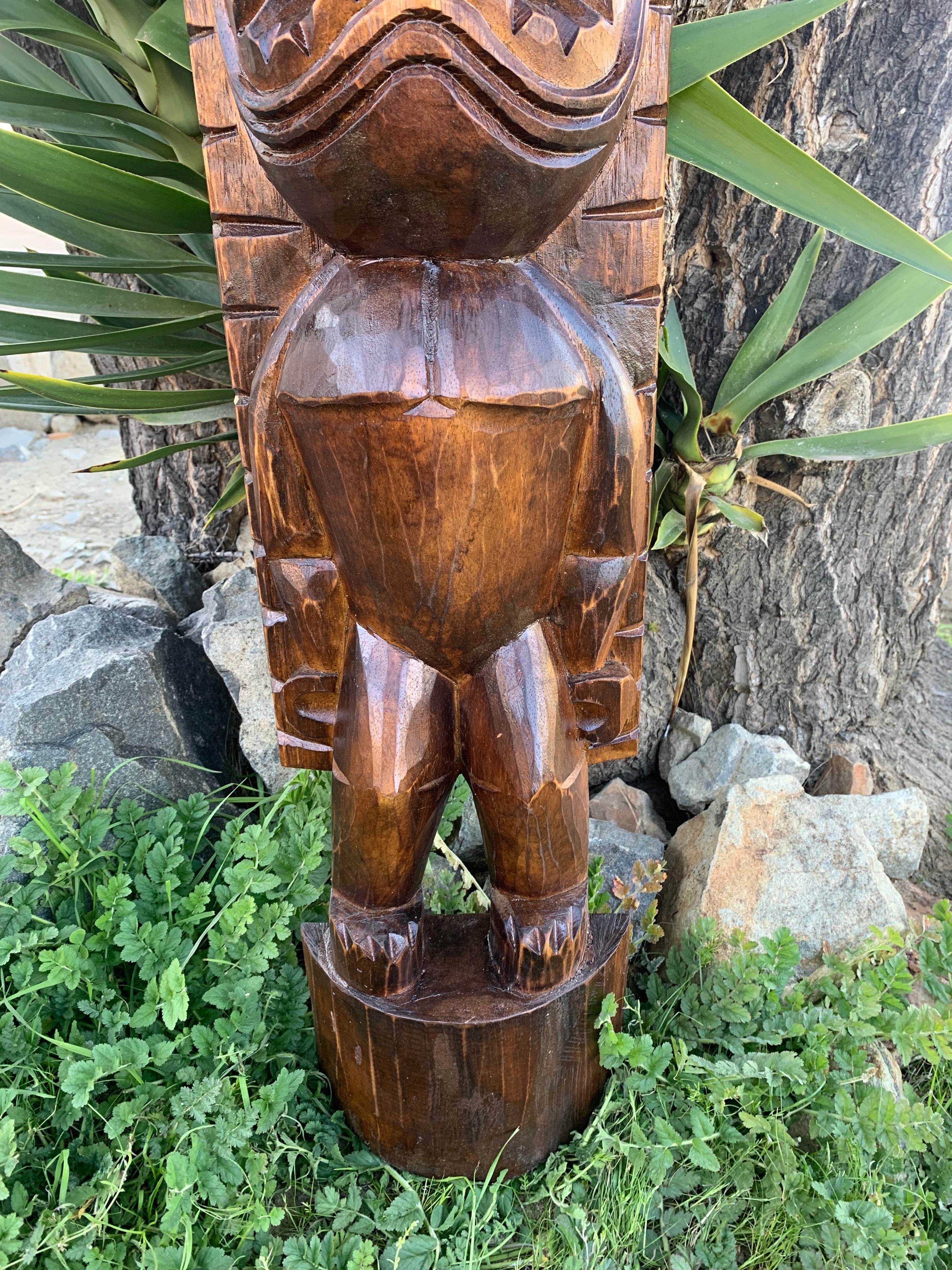 Wooden carved humanoid totem statue outdoors among greenery and rocks