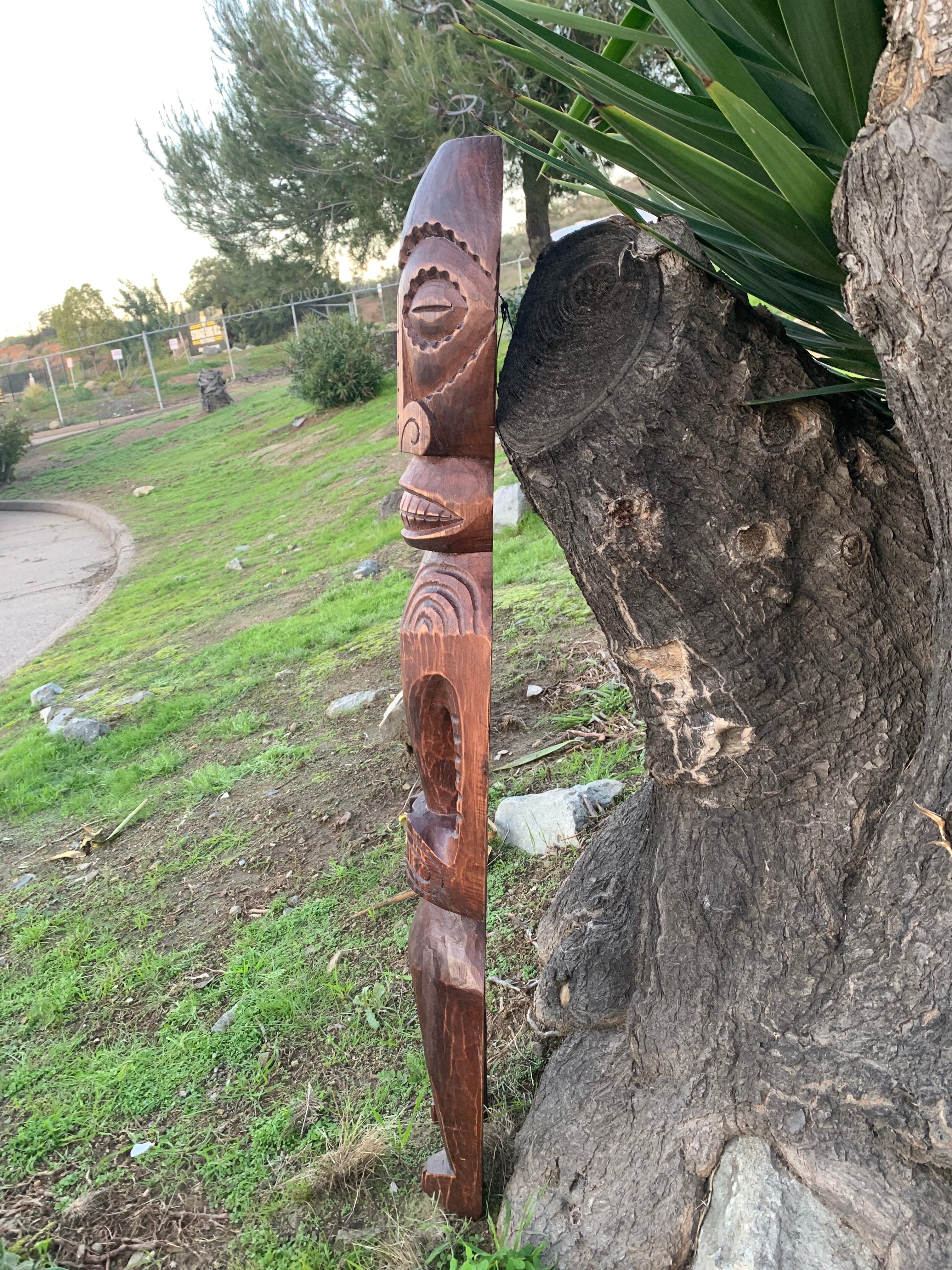 Carved wooden totem pole leaning against a tree in a park setting
