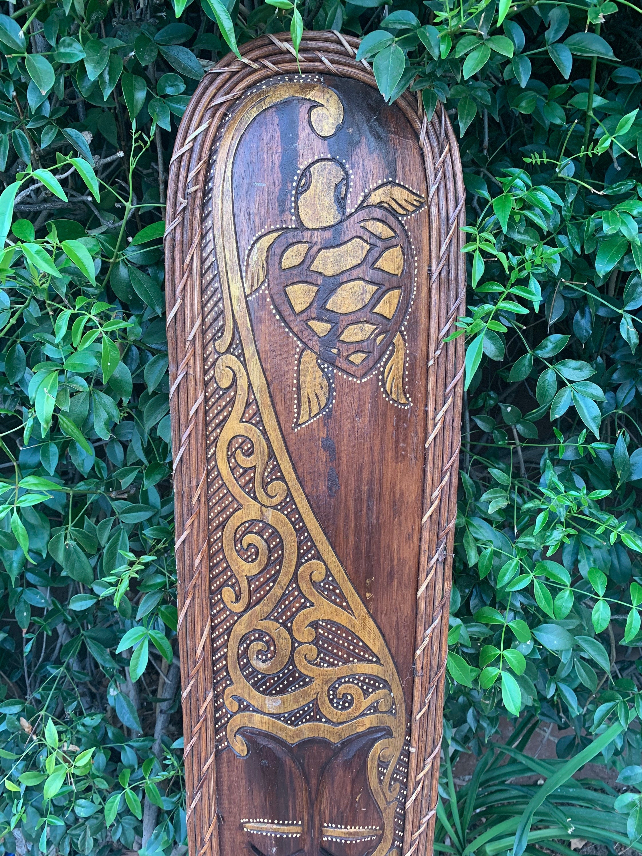 Wooden carved panel featuring a stylized turtle and ornate scrollwork, set against green foliage.