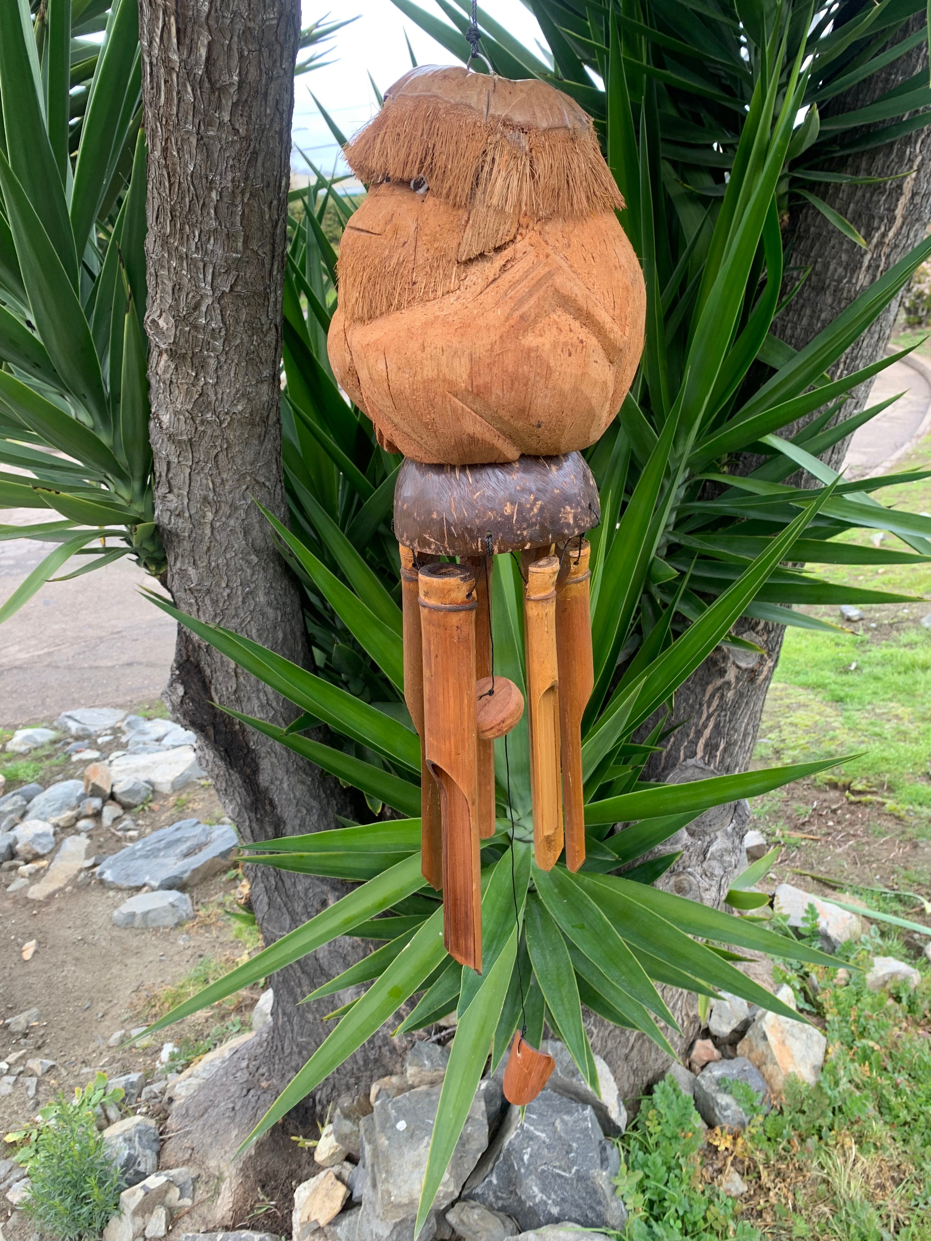 Carved wooden owl wind chime with bamboo tubes hanging from a tree in a garden