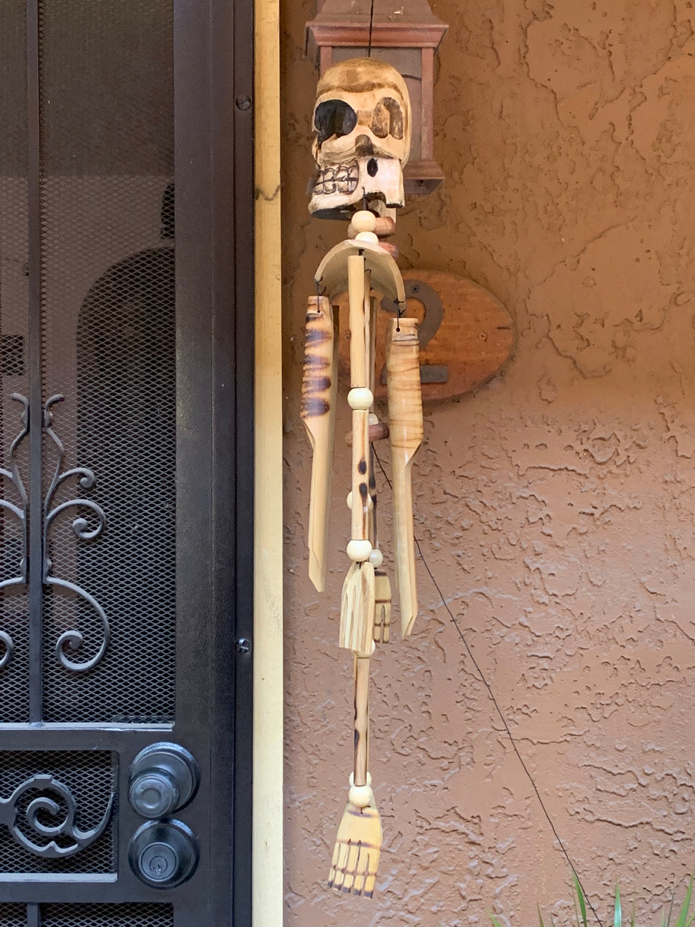 Wooden skeleton hanging decoration with skull head and string limbs beside a door.