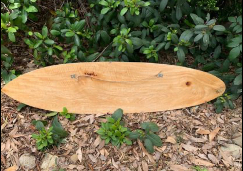 wooden surfboard resting on mulch amid green shrubs