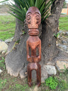carved wooden tiki figure leaning against a tree in a garden